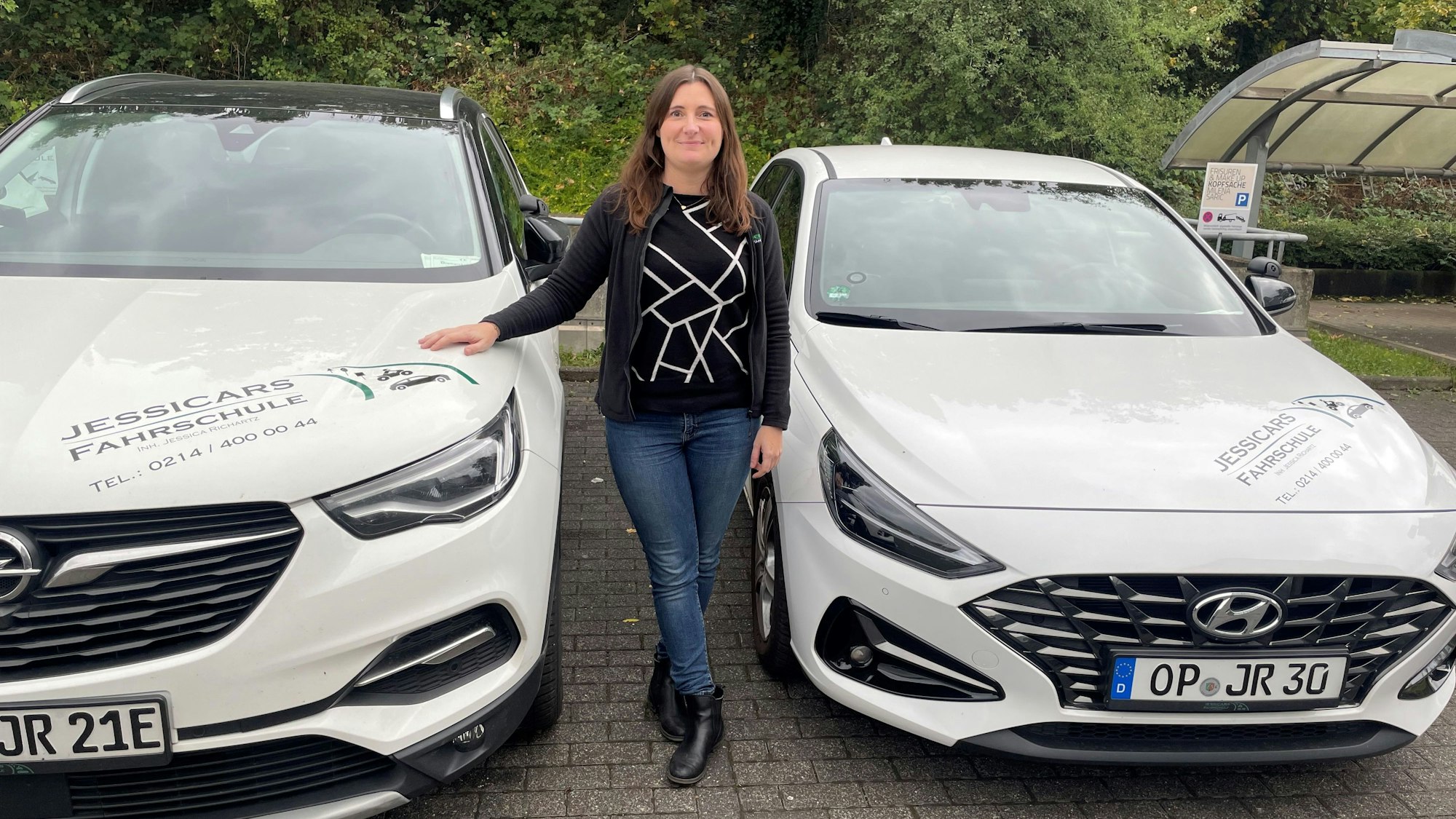 Jessica Richartz steht zwischen zwei Fahrschulautos.