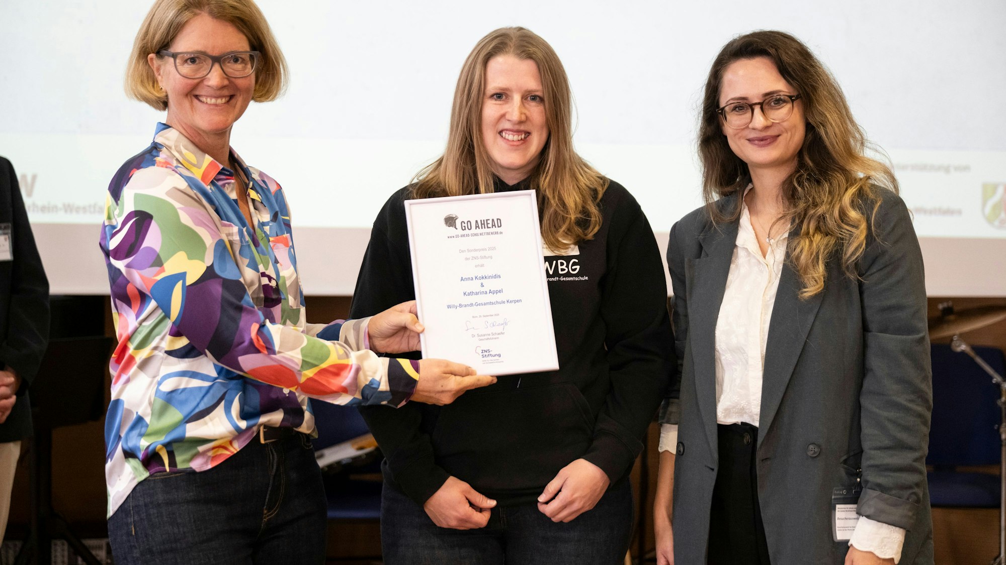 Das Foto zeigt drei Frauen bei der Übergabe einer Urkunde.