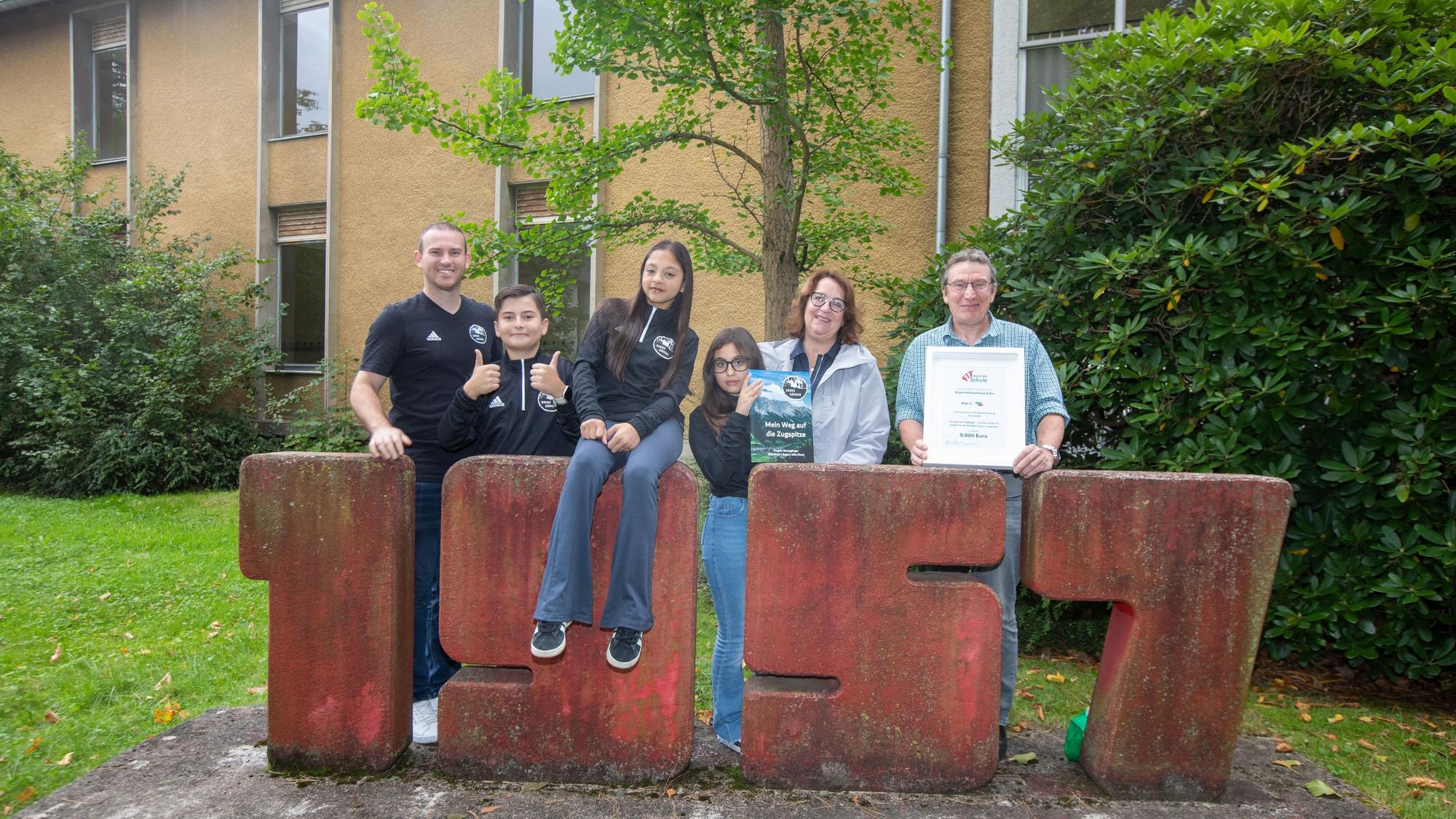 Schüler und Lehrer stehen vor einem Schulgebäude.