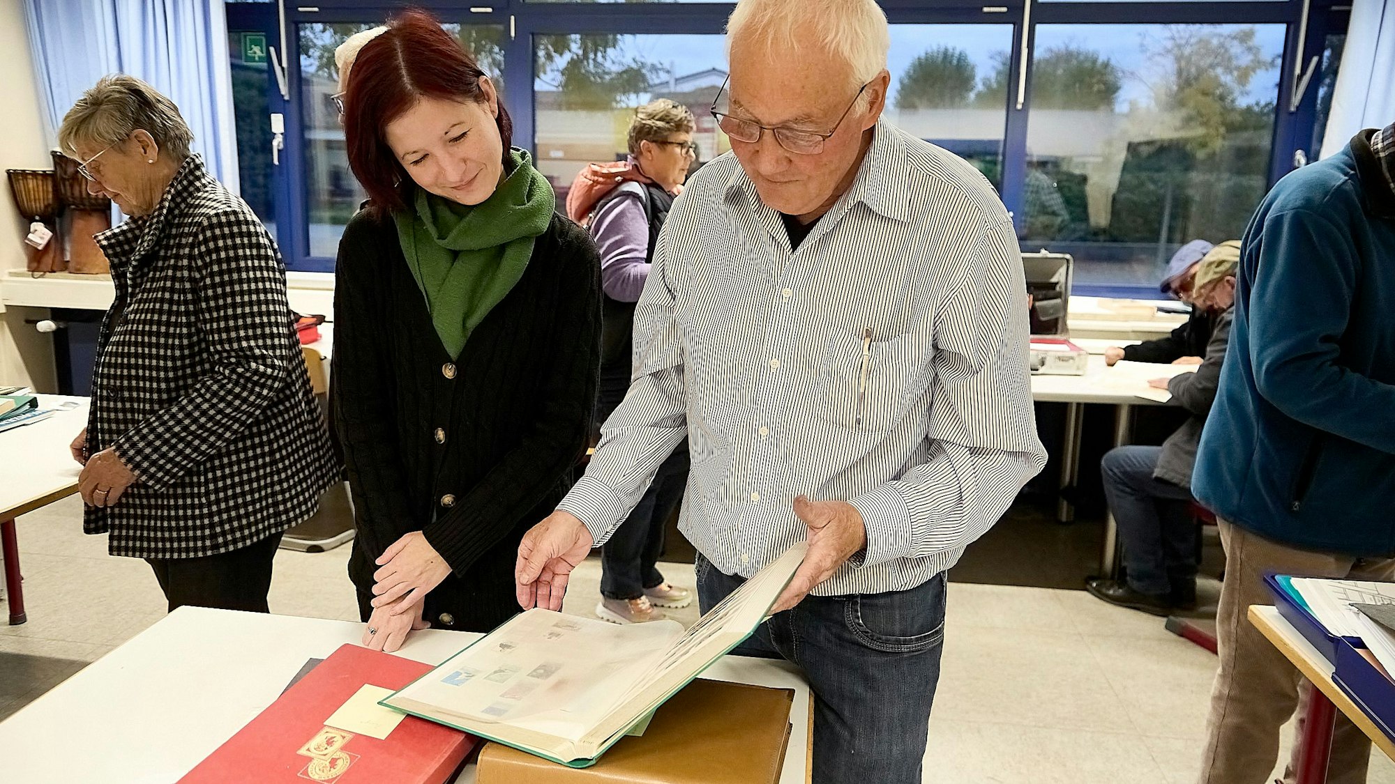 Ein Mann und eine Frau schauen in Alben, die eine Briefmarkensammlung beinhalten.