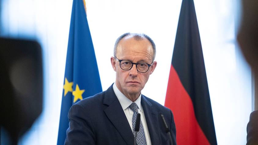 Friedrich Merz steht hinter zwei Mikrofonen und vor einer Deutschland- sowie einer EU-Fahne