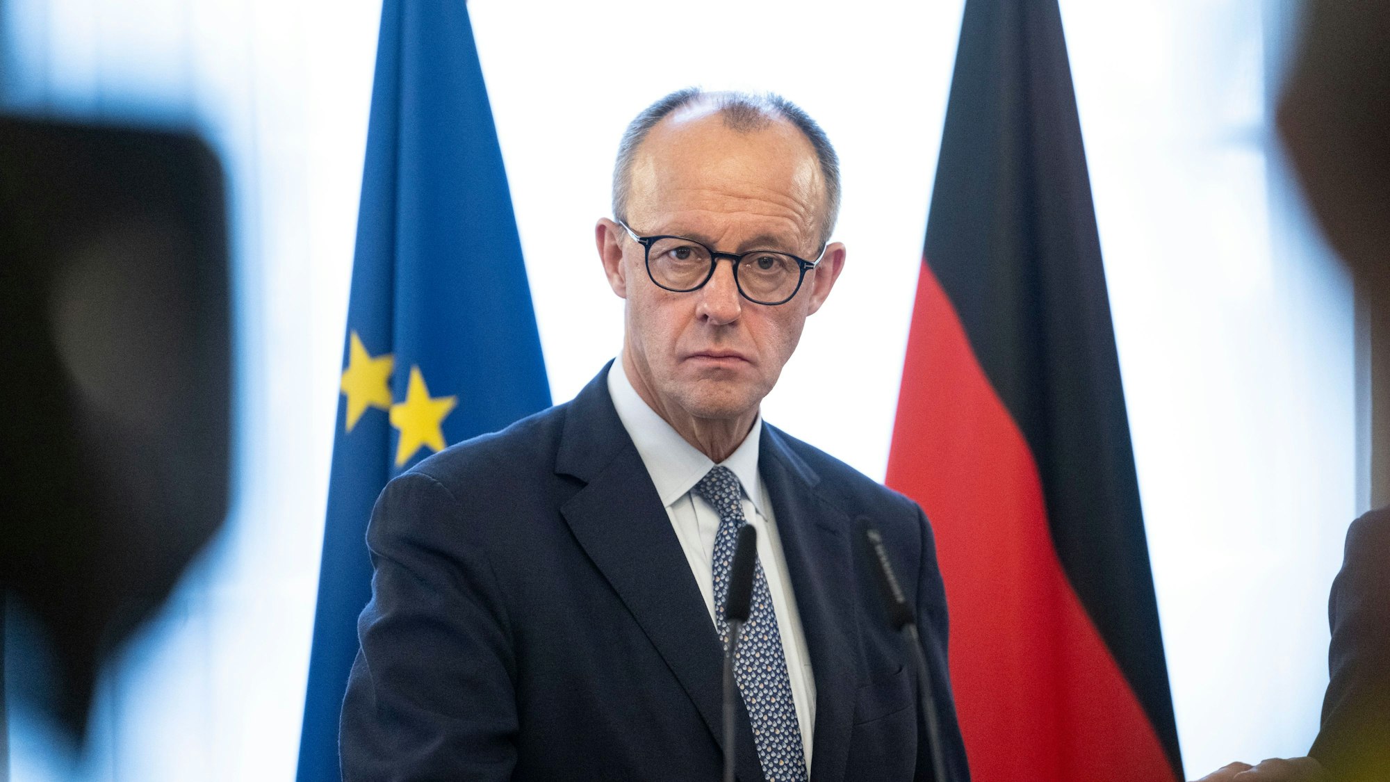 Friedrich Merz steht hinter zwei Mikrofonen und vor einer Deutschland- sowie einer EU-Fahne