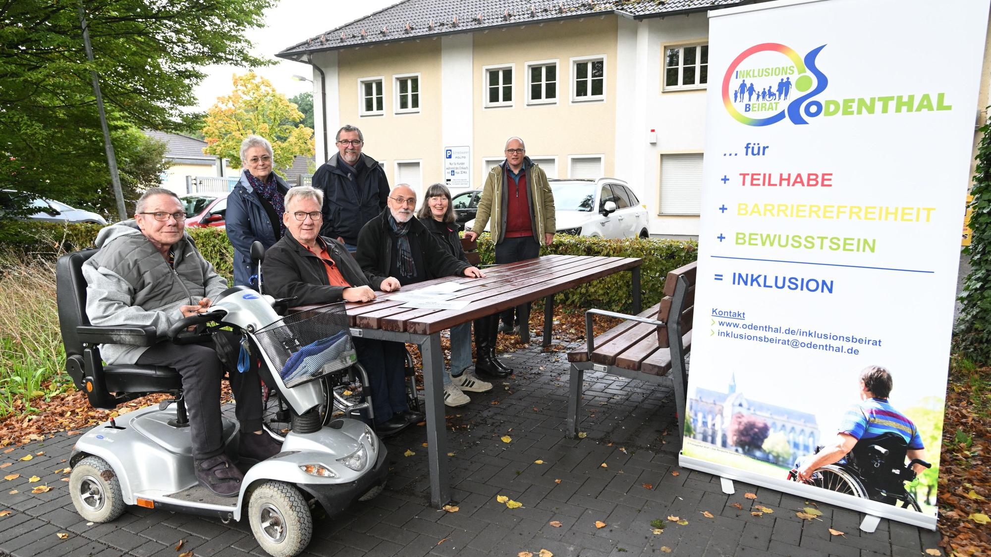 Eine behindertengerechte Sitzecke in einer Grünanlage. Zwei Rollstuhlfahrer sitzen daran.