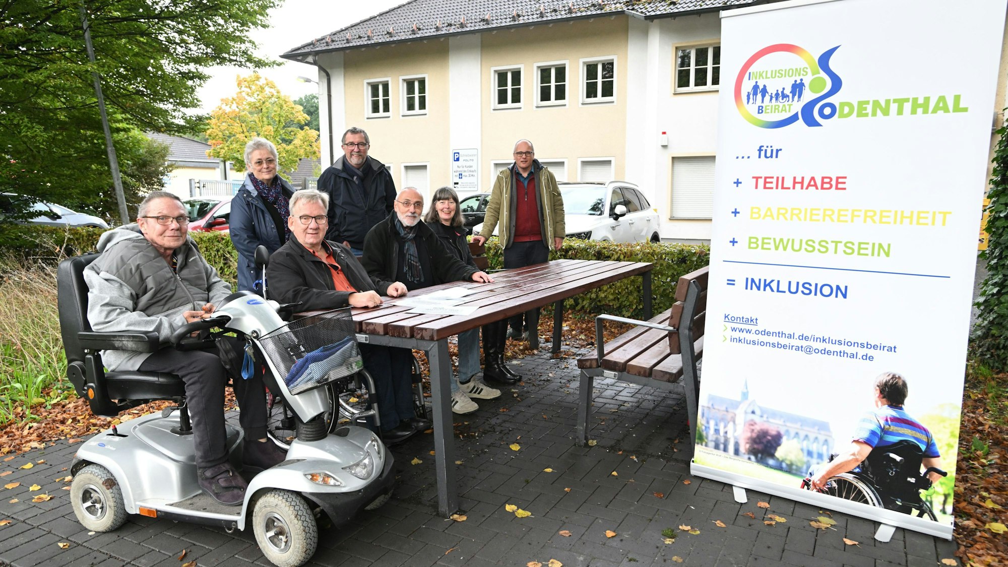 Eine behindertengerechte Sitzecke in einer Grünanlage. Zwei Rollstuhlfahrer sitzen daran.