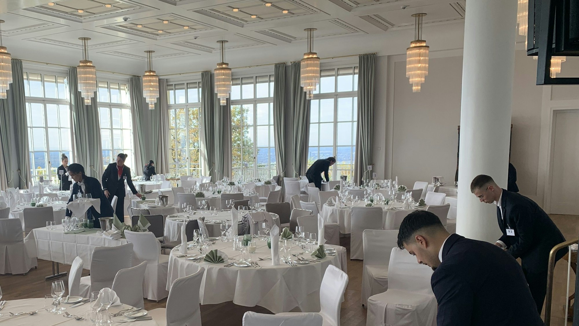 Mehrere Personen decken und dekorieren Tische in einem großen Saal.