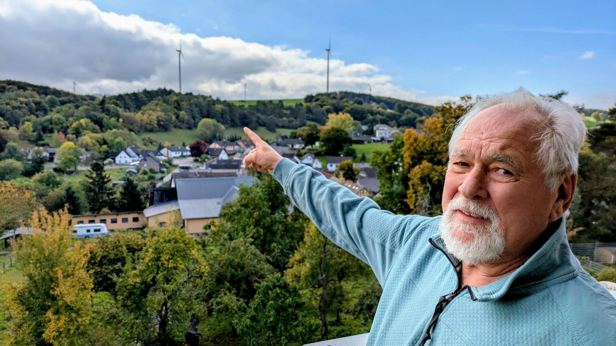 Der Kallmuther Ortsbürgermeister Robert Ohlerth deutet auf den südlich des Ortes gelegenen Windpark am Ravelsberg.