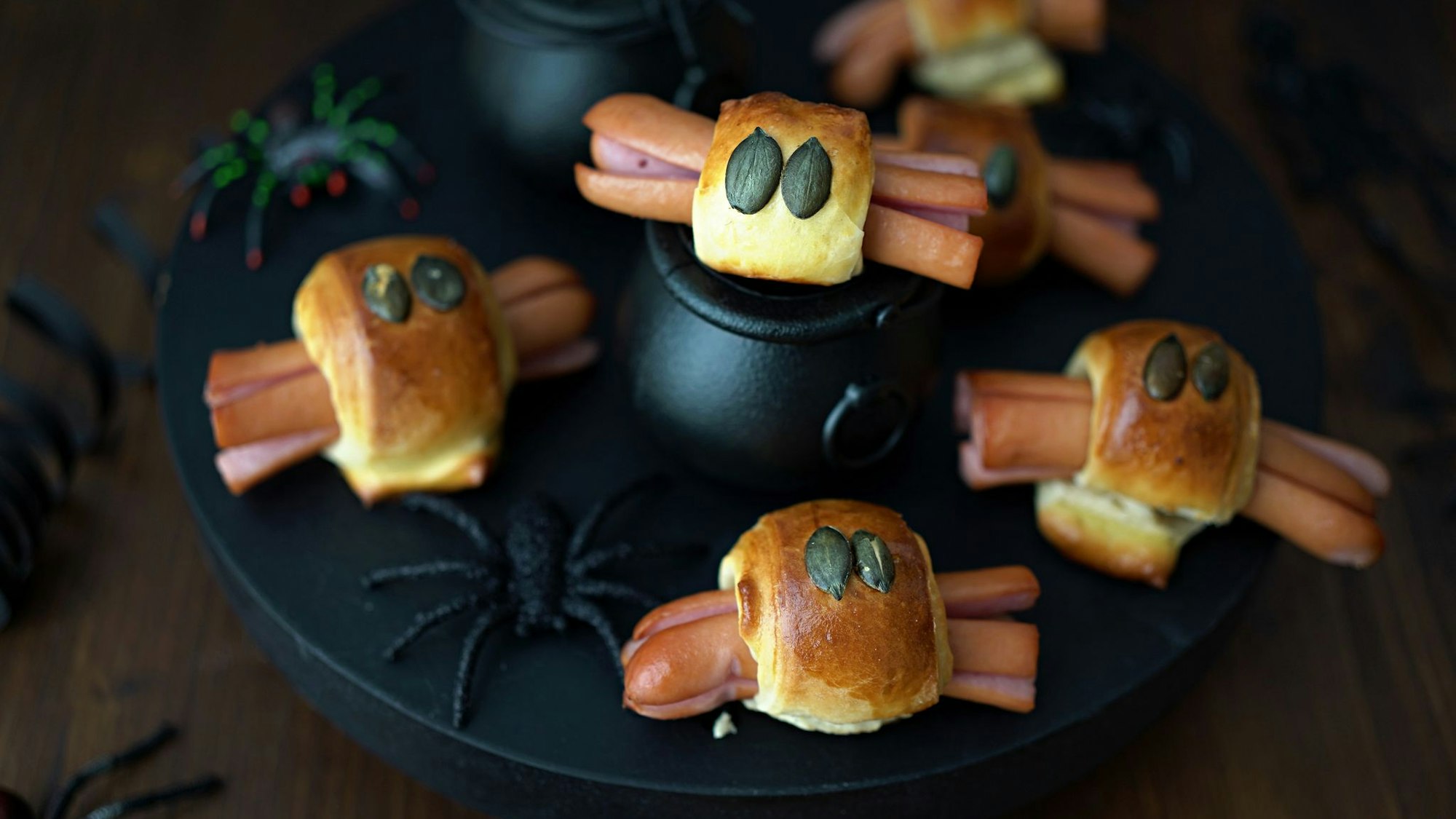 Für die Würstchenspinnen werden die an den Enden eingeschnittenen Wienerstückchen mit Teigstreifen umwickelt. Darauf drückt man je zwei Kürbiskerne als Augen und schiebt das Ganze in den Backofen.