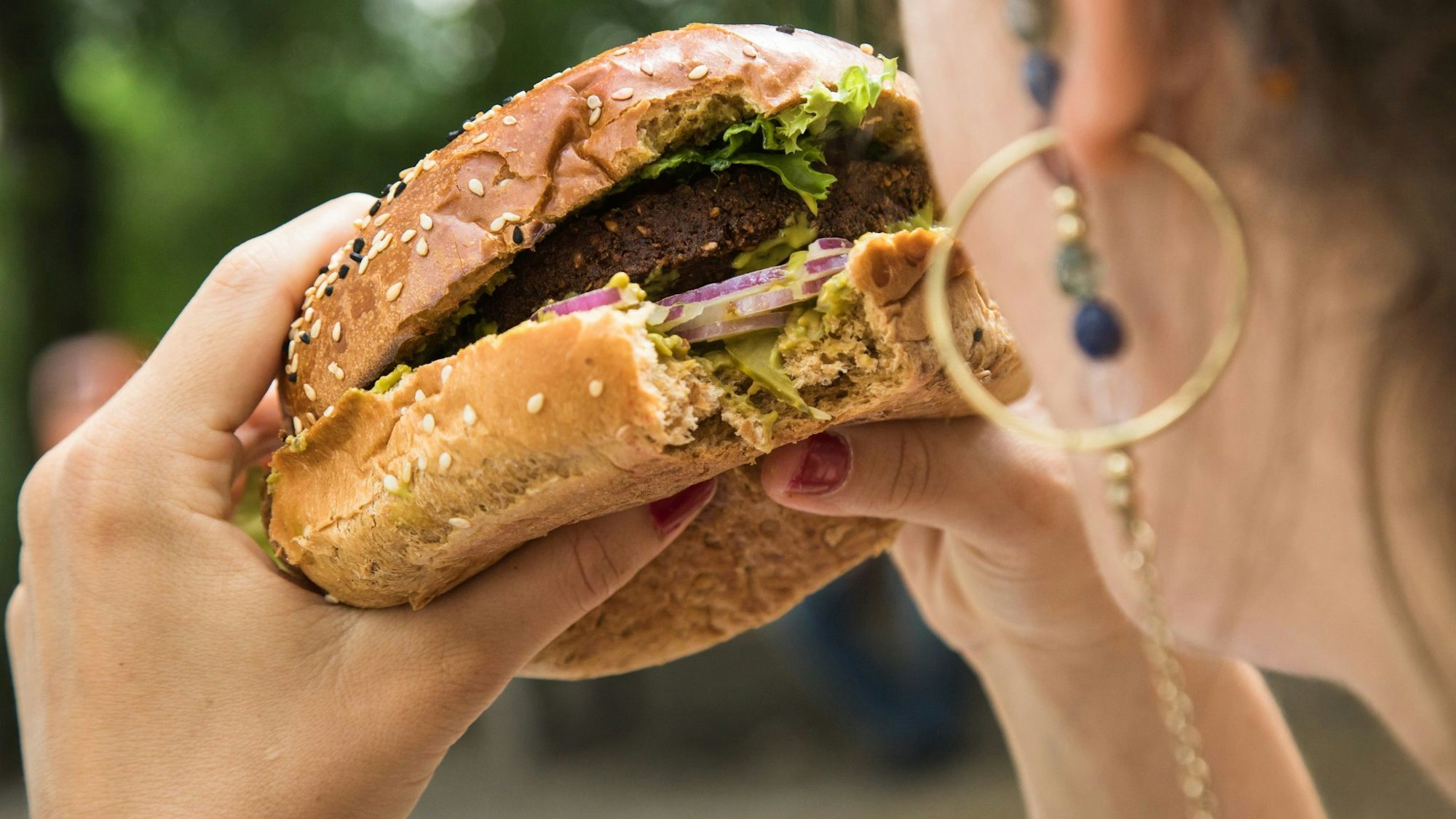Das Gesicht einer Frau wird von hinten gezeigt, sie hält einen Burger in den Händen.