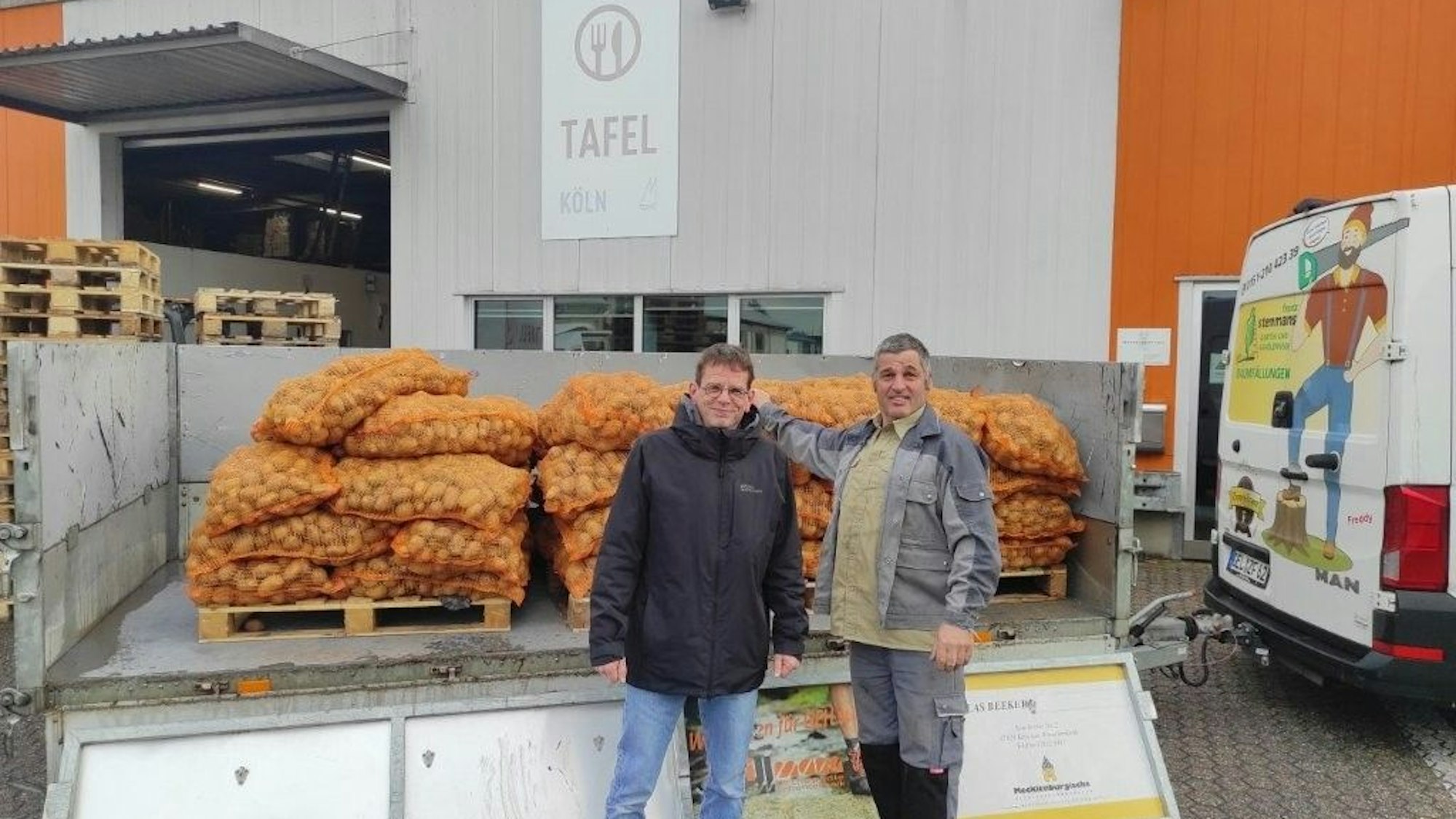 Zwei Männer stehen vor einem Anhänger mit vielen Kartoffelsäcken.