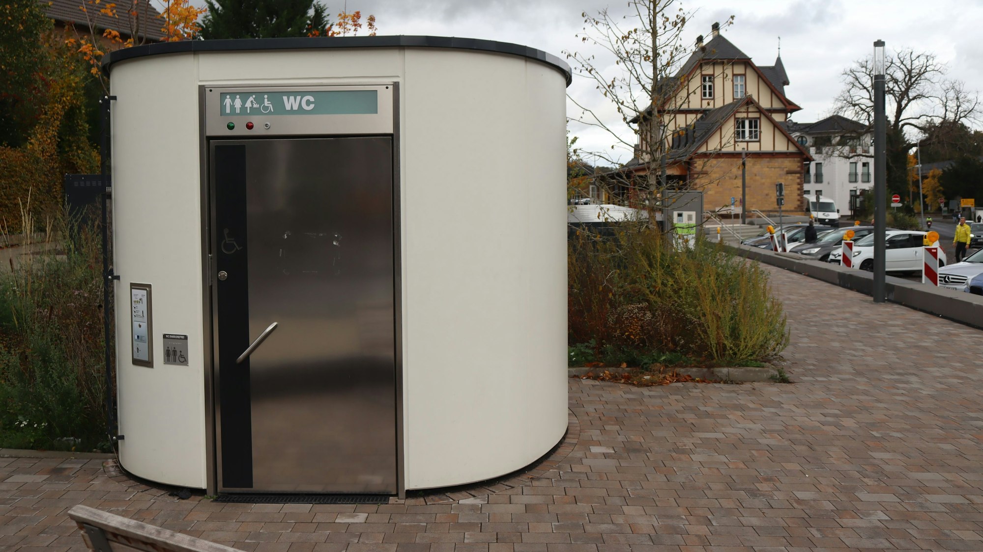 Ein Toilettenhäuschen steht im Vordergrund, im Hintergrund ist das Bahnhofsgebäude zu sehen.