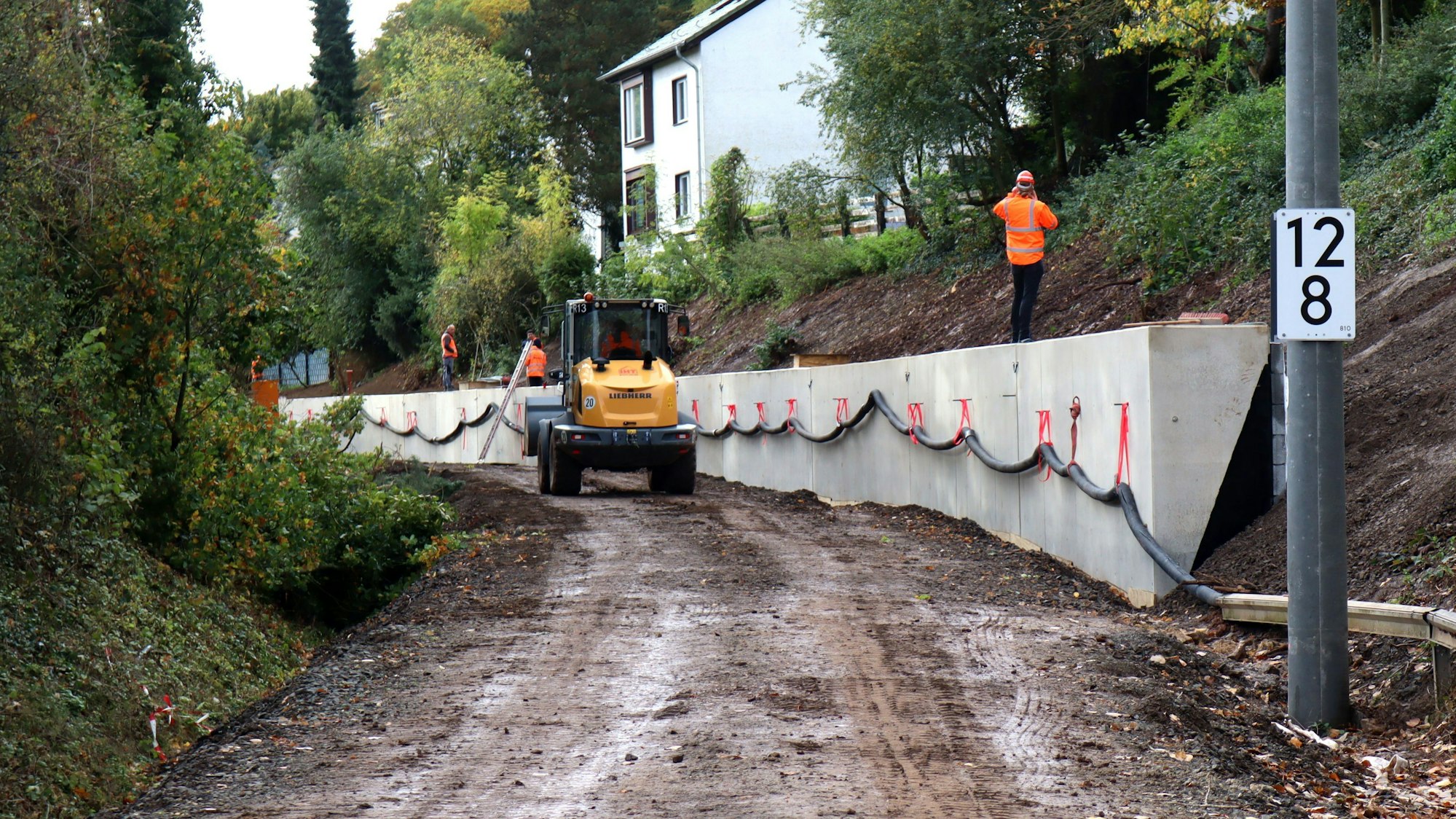 Ein Bagger fährt entlang der Stützmauer. Die Gleise in dem Bereich der Erfttalbahn fehlen. Auf der Mauer steht ein Arbeiter und telefoniert.