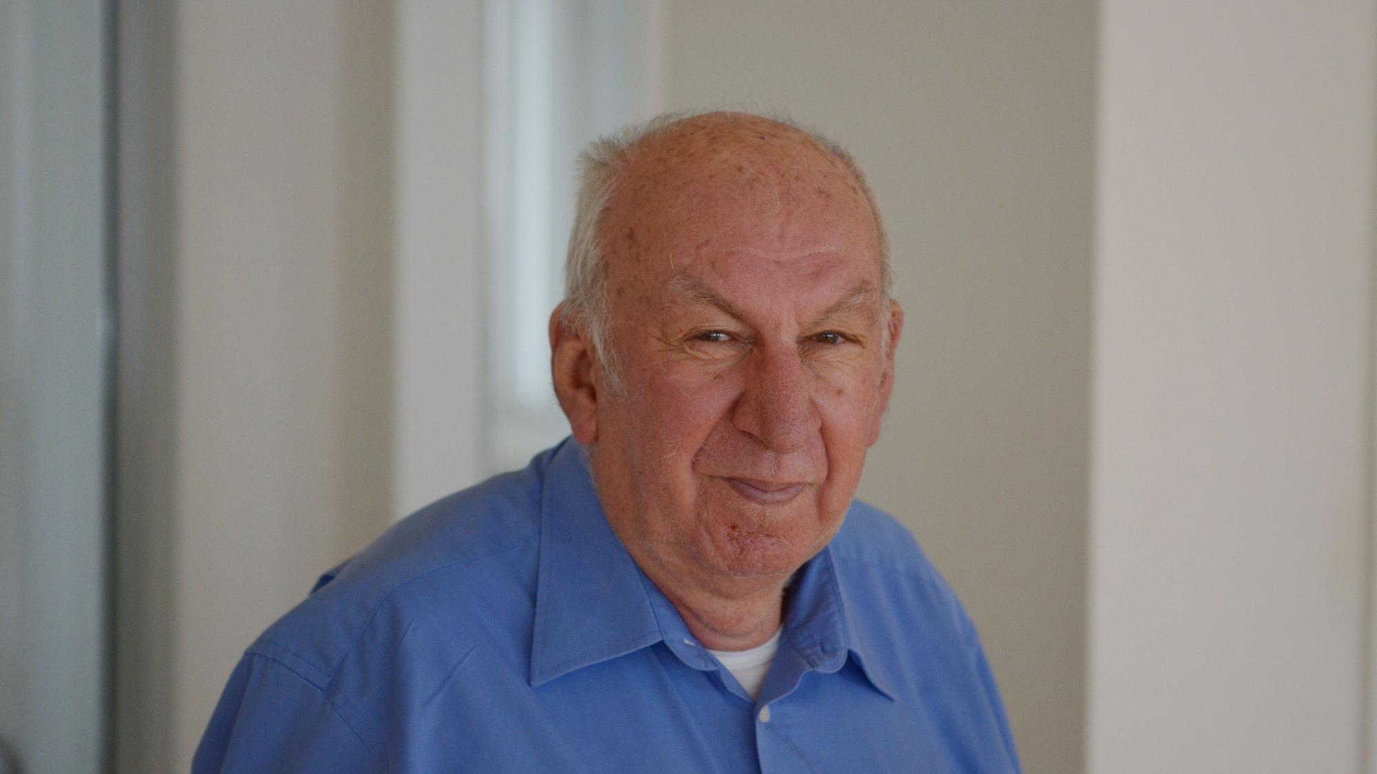 Das Porträt zeigt Josef Schleser, der ein blaues Hemd trägt, in einem Raum mit hellen Wänden.