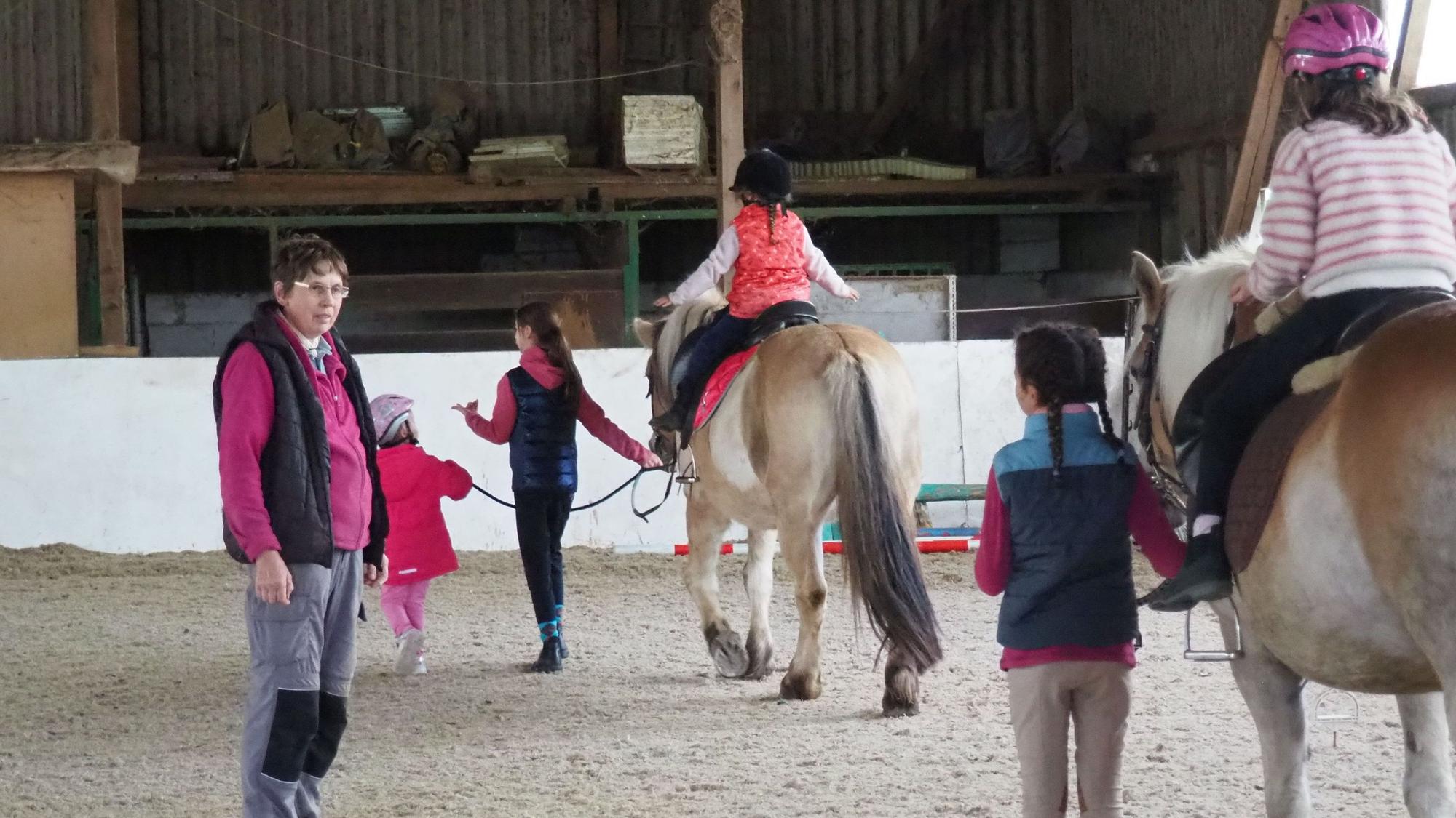 In der Reithalle steht Helga Lagier und schaut Kindern zu, die auf Pferden reiten lernen.