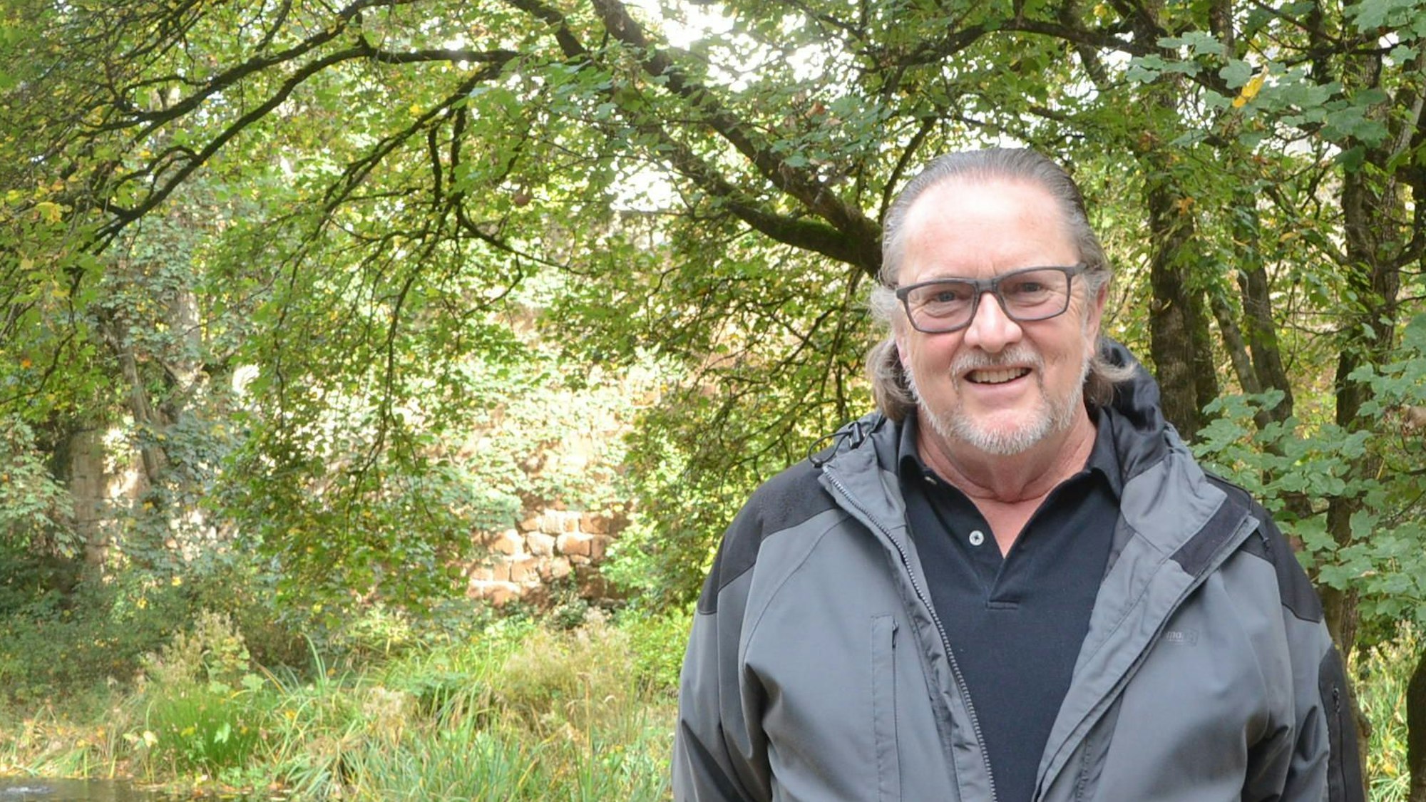 Ein Mann steht vor einem Hintergrund aus Bäumen in einem Park.