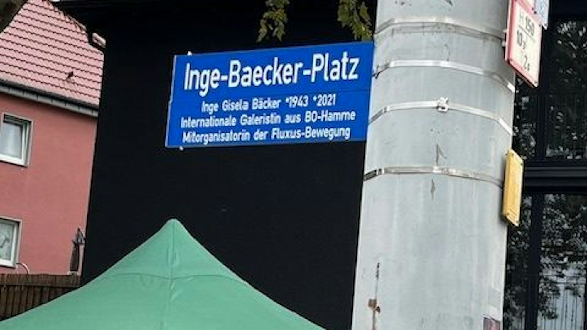 Ein Schild mit der Aufschrift Inge-Baecker-Platz hängt an einem Mast.