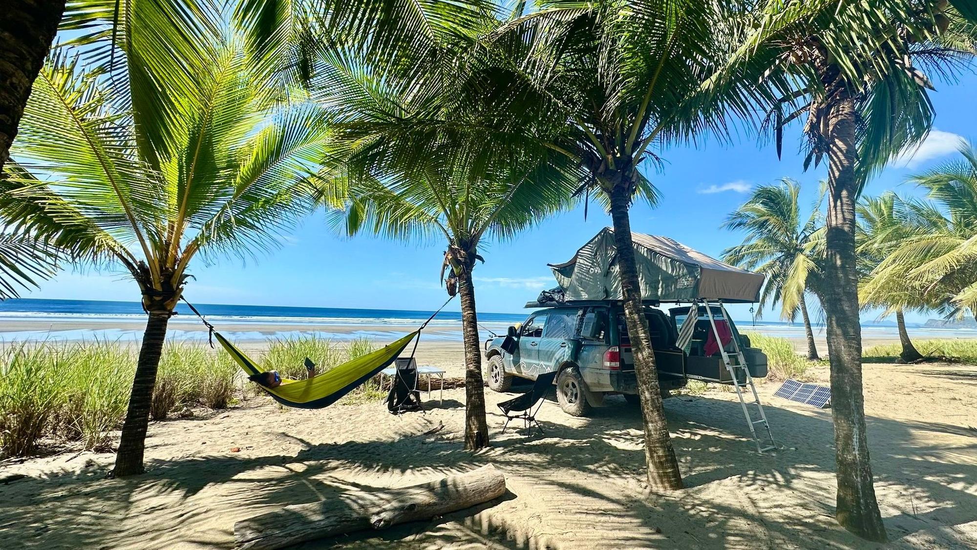 Ein zum Reisemobil umgebauter Mitsubishi Pajero steht unter Palmen an einem Strand in der Karibik.
