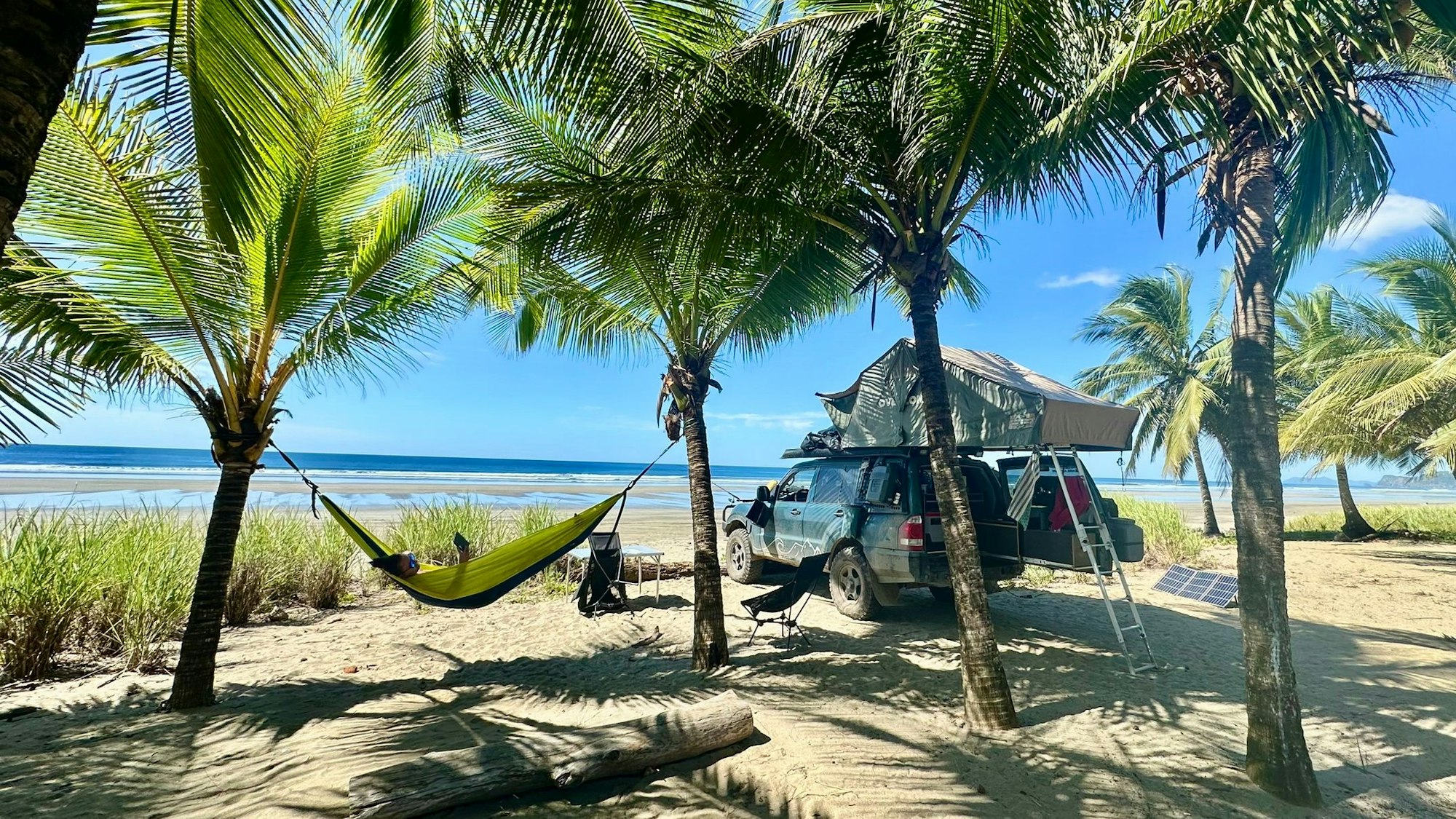 Ein zum Reisemobil umgebauter Mitsubishi Pajero steht unter Palmen an einem Strand in der Karibik.
