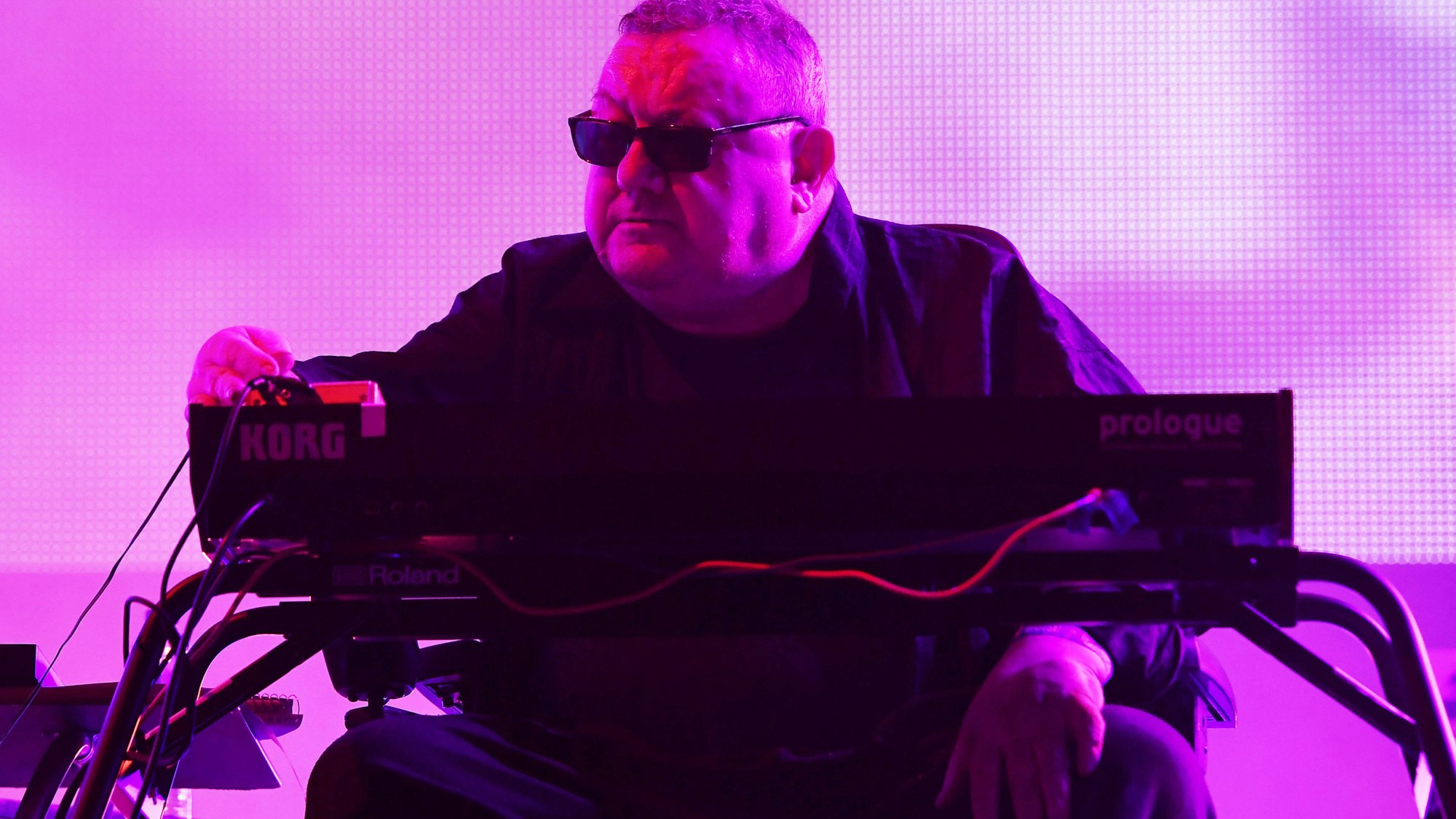 Dave Ball spielt Keyboard unter violettem Bühnenlicht.