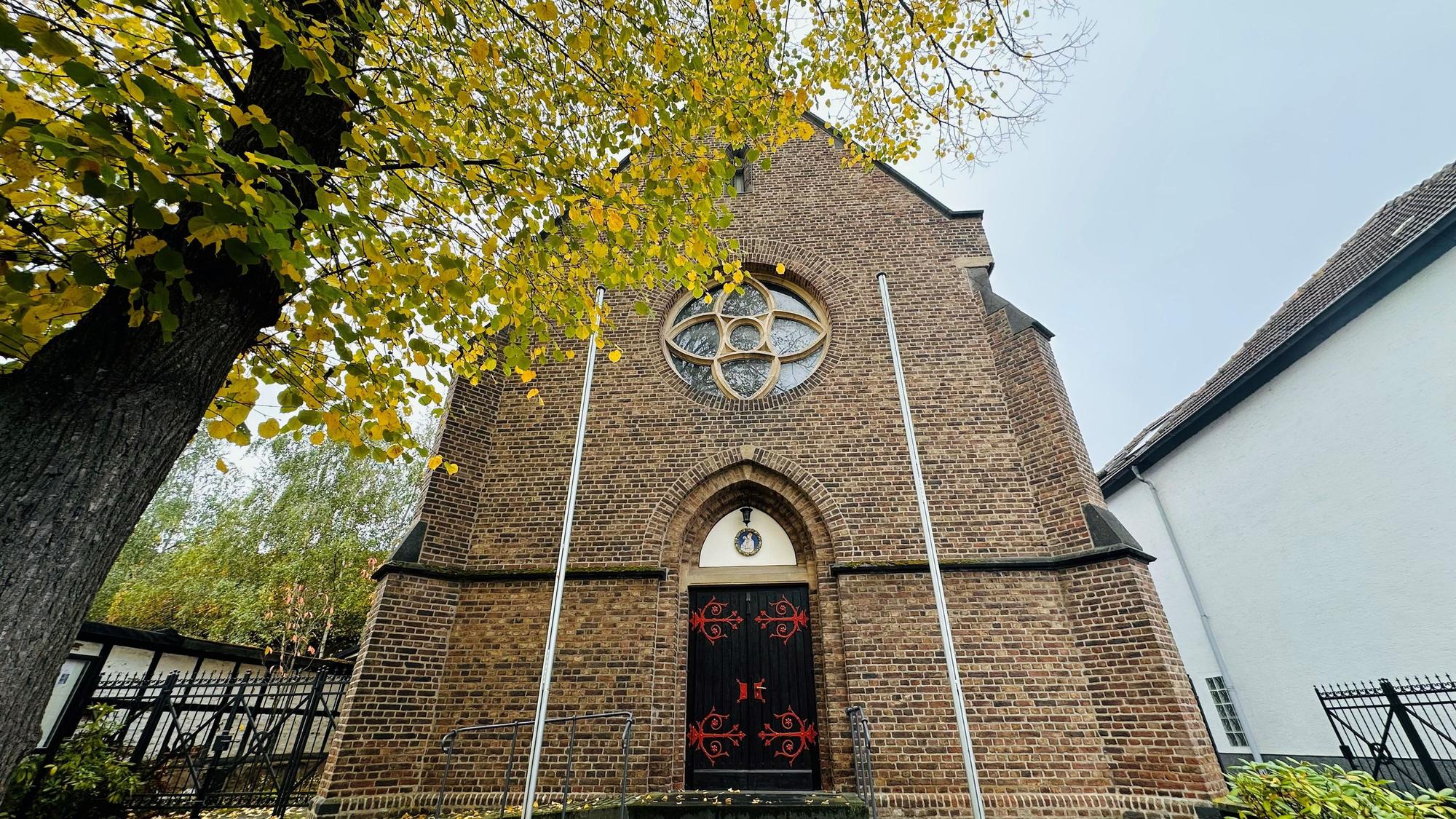 Zu sehen ist eine Kirche, davor steht ein Baum.