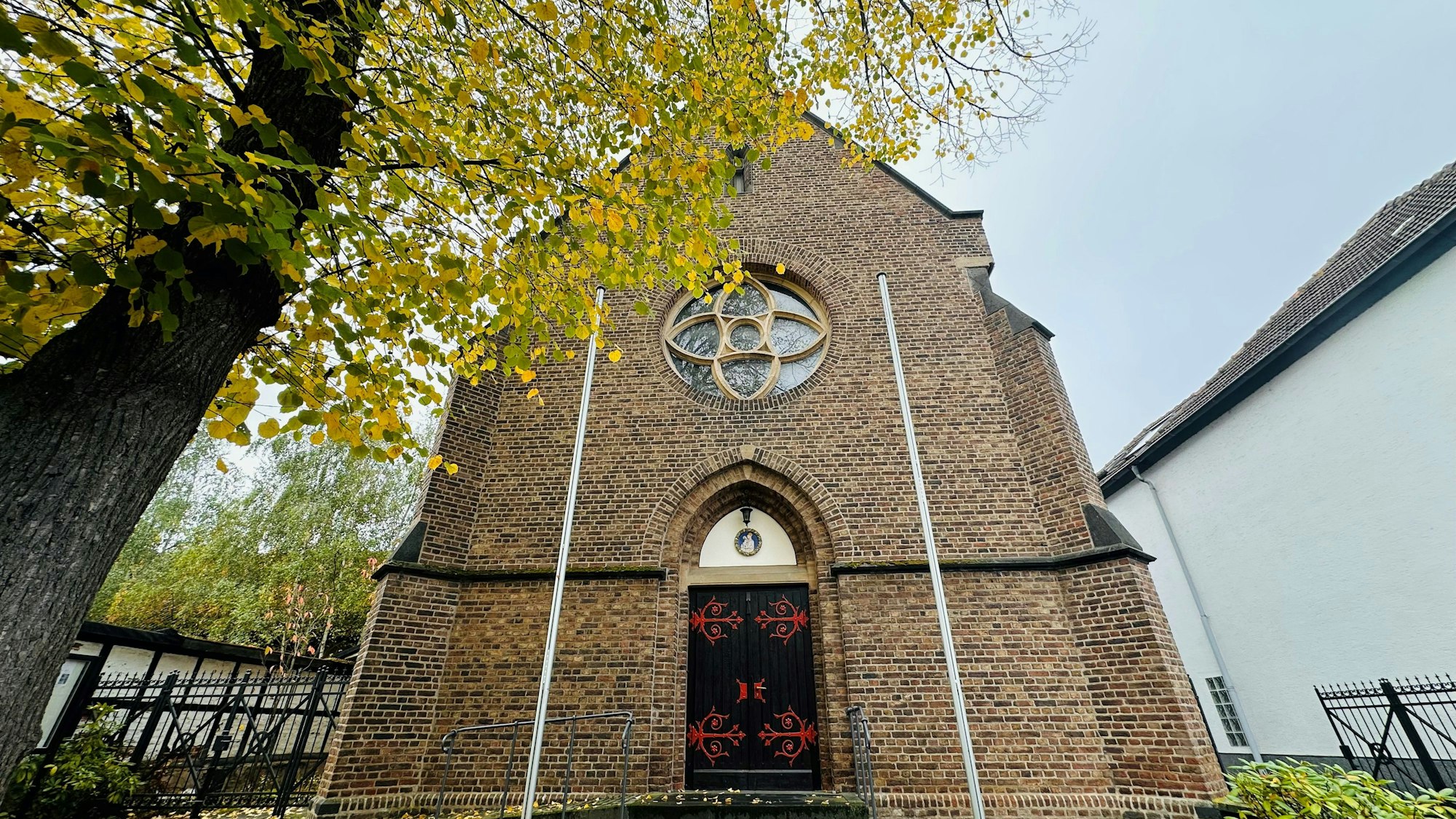 Zu sehen ist eine Kirche, davor steht ein Baum.