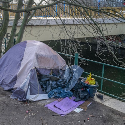 Ein Obdachlosenzelt mit Habseligkeiten am Kanal unter einer städtischen Brücke.