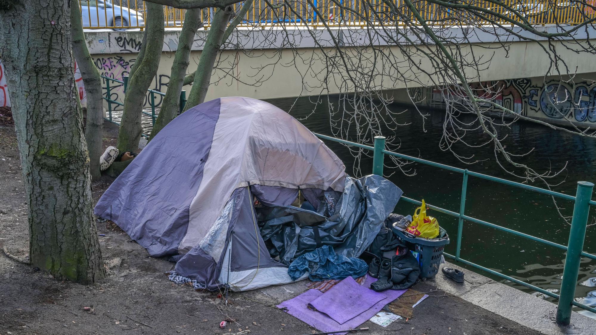 Ein Obdachlosenzelt mit Habseligkeiten am Kanal unter einer städtischen Brücke.