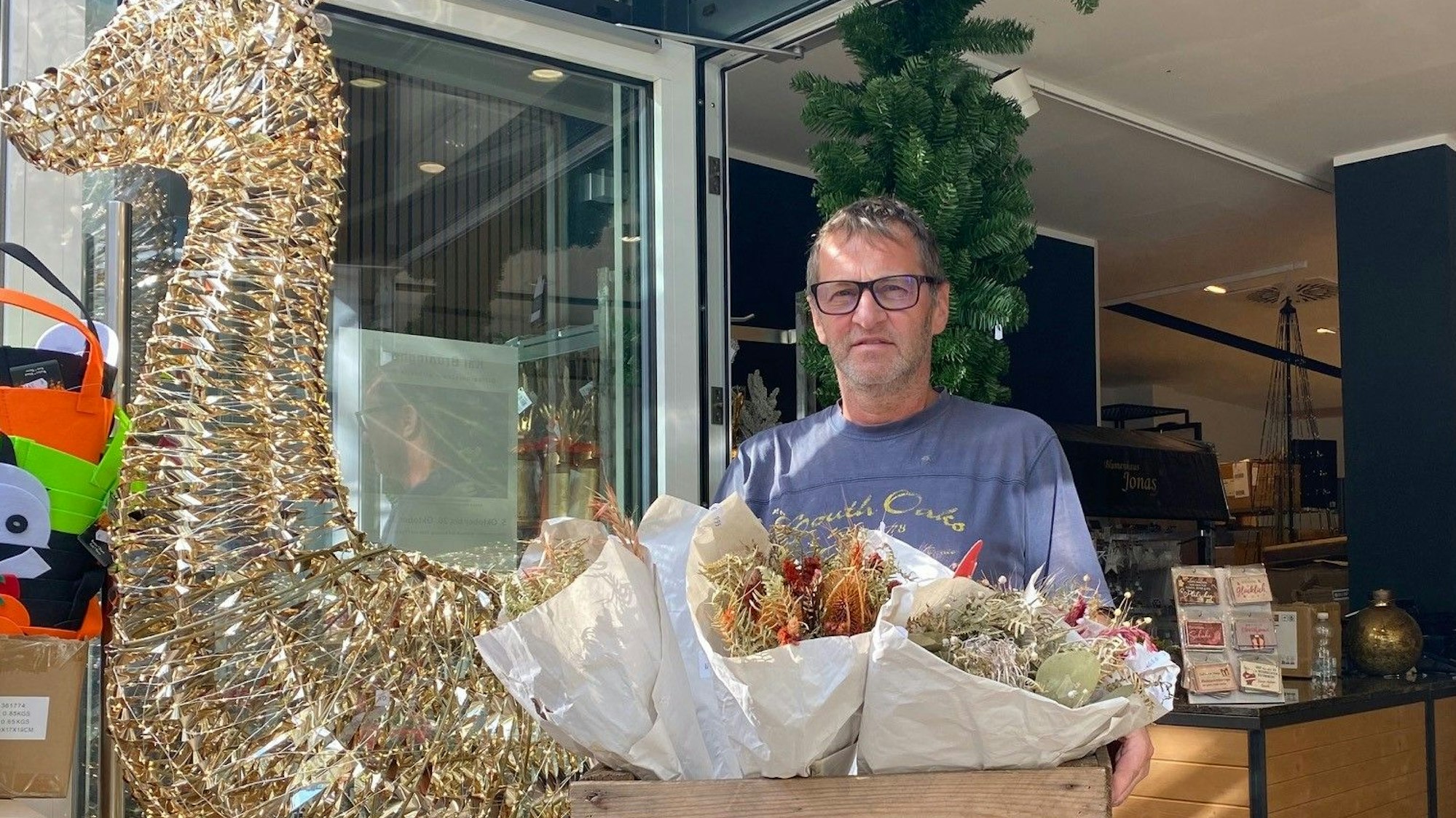 Zu sehen ist Dirk Jonas, der eine Holzkiste mit Blumengestecken trägt.