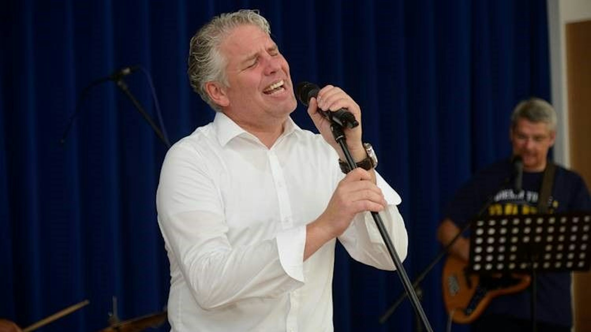 Ein Mann mit weißem Hemd singt in ein Mikrofon.