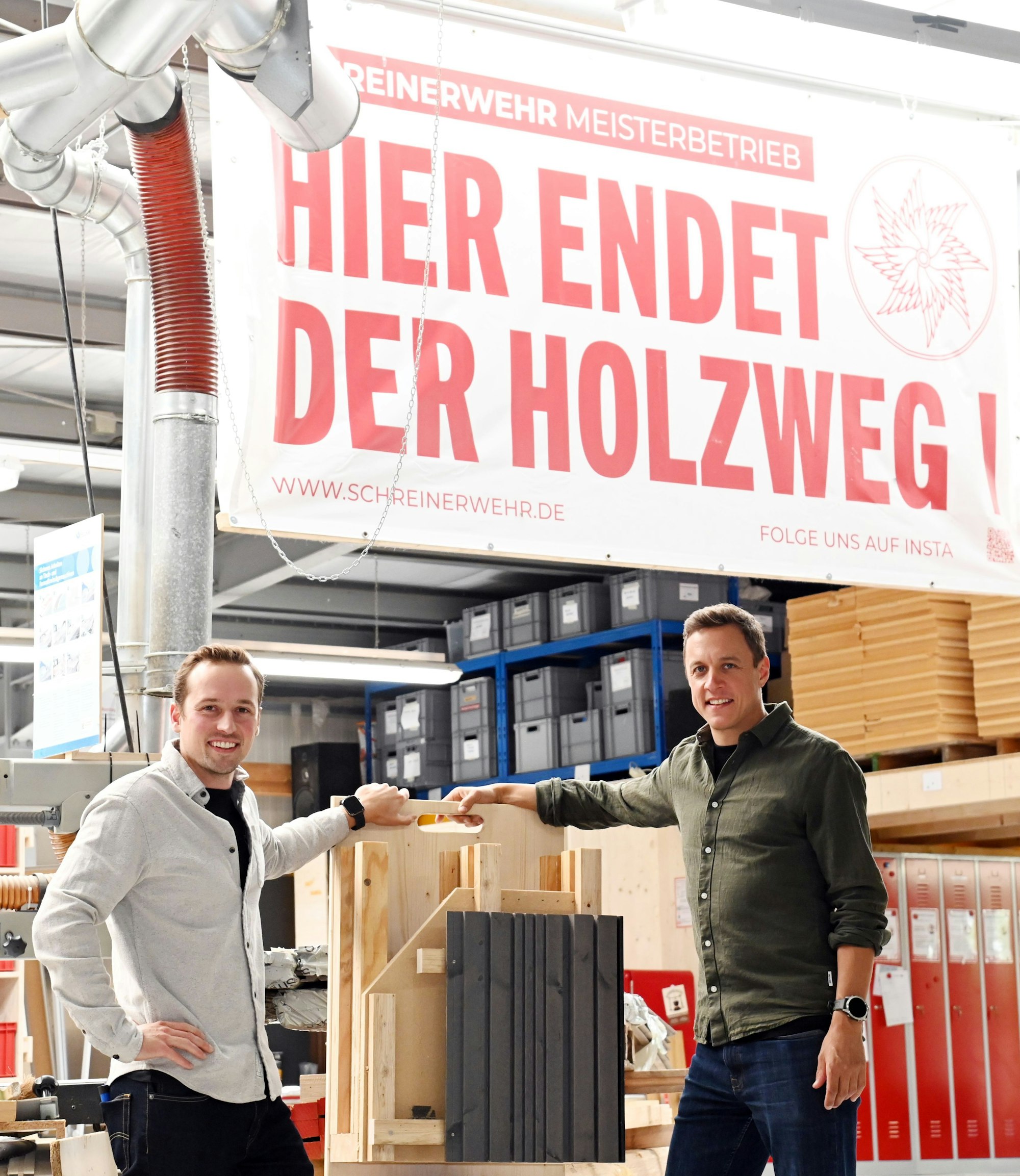 Zwei Männer stehen an einem Stück Holz.