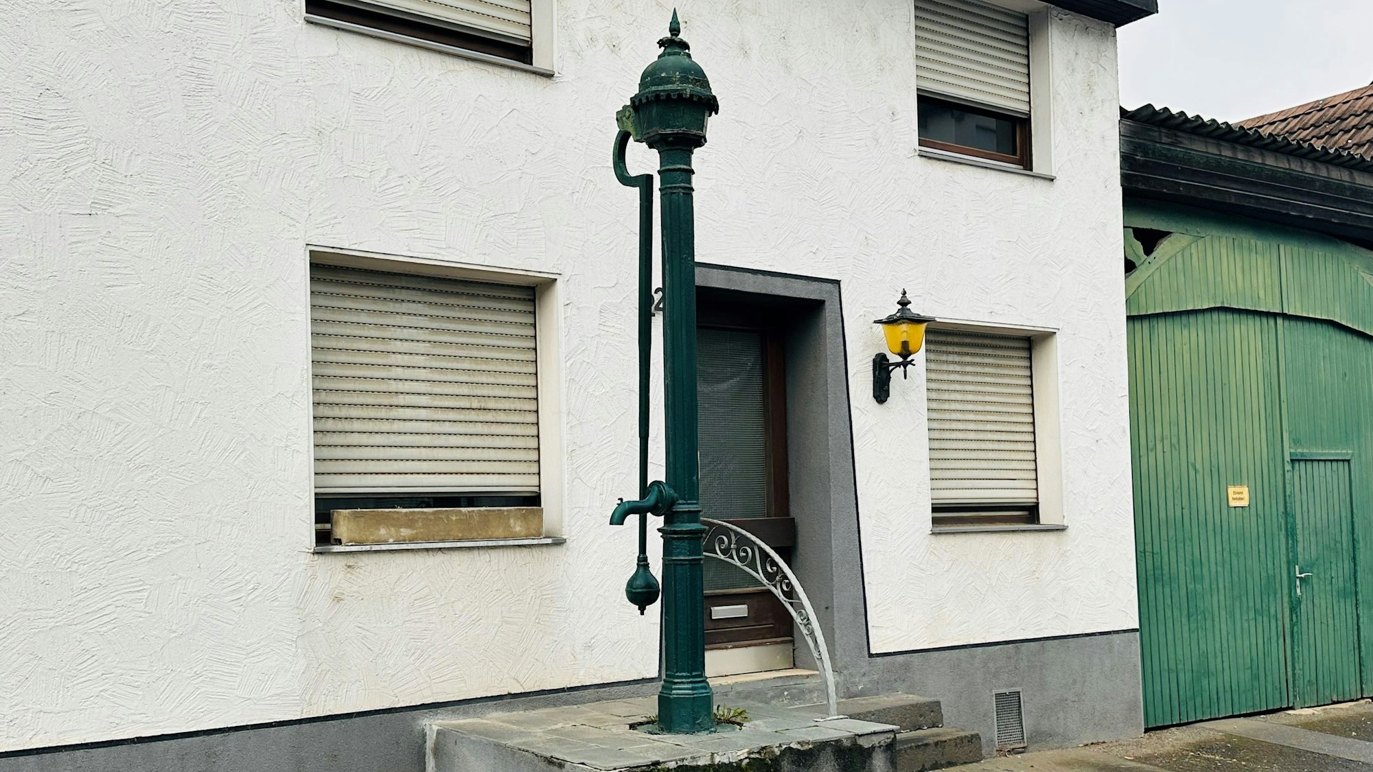 Zu sehen ist eine gusseiserne Pumpe vor einem Haus.