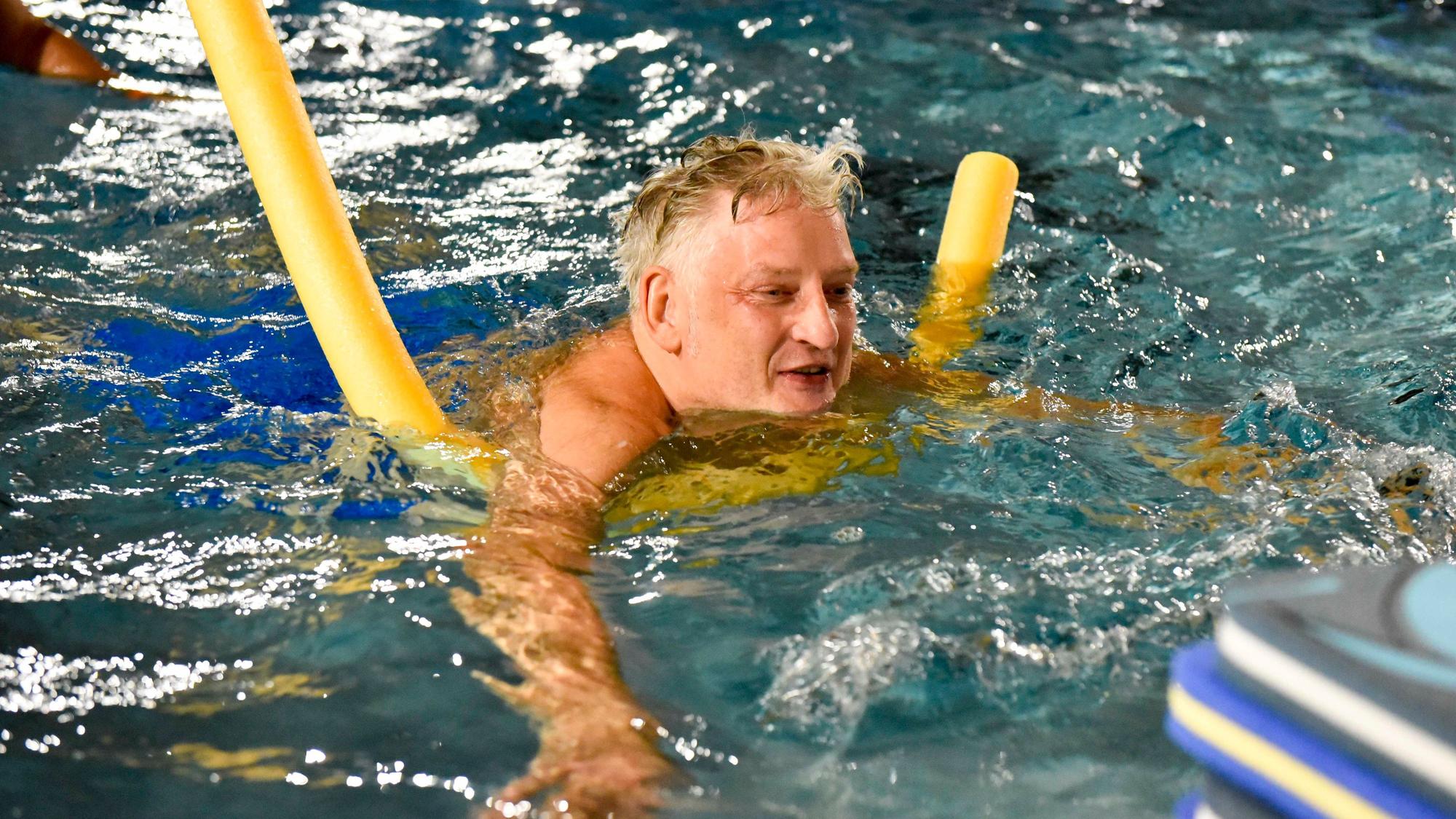 Das Bild zeigt den Mann mit einer Schwimmnudel im Becken.