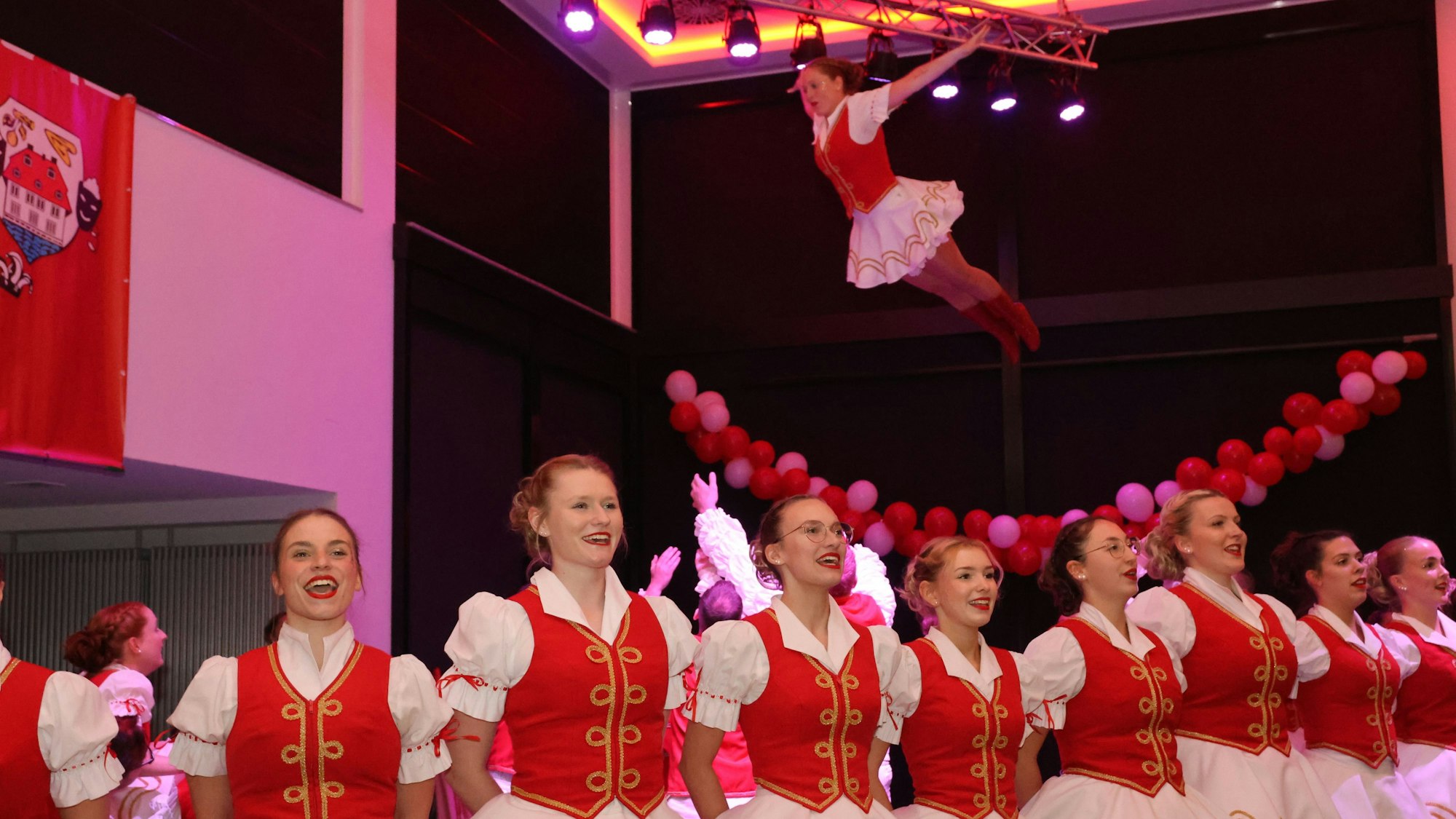 Im Vordergrund stehen Tänzerinnen. Im Hintergrund wird eine Tänzerin nach einem Sprung aufgefangen.