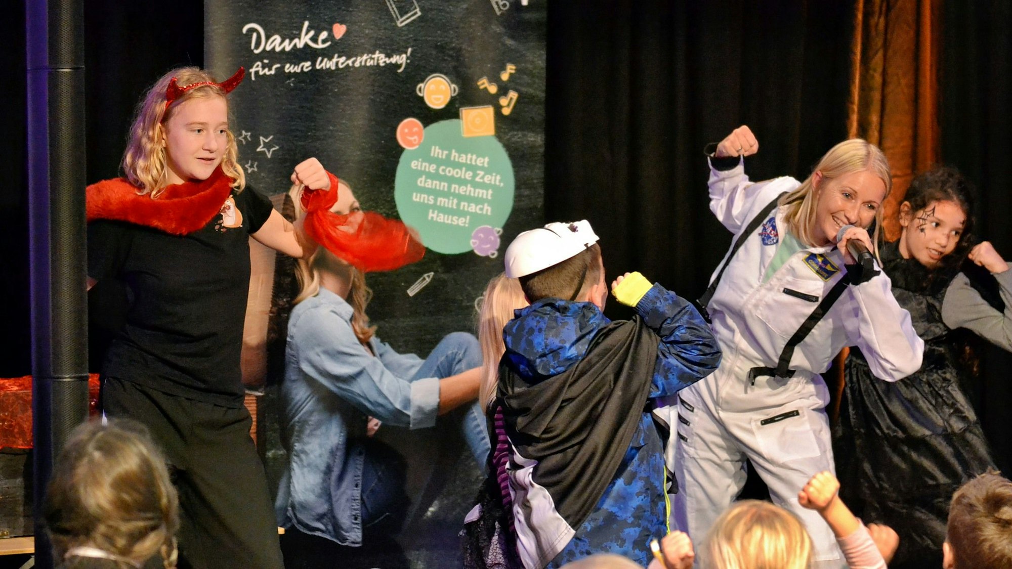 Mehrere Kinder tanzen vor einem Plakat.