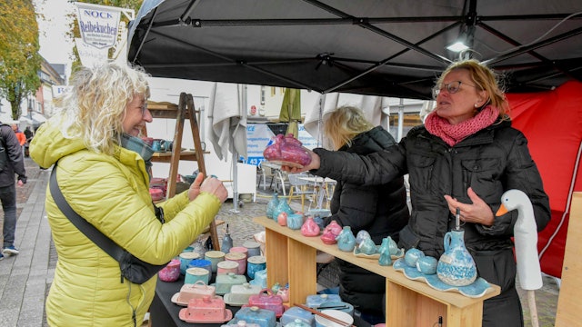 Zu sehen ist eine Frau, die an einem Stand mit Töpferware einkauft.