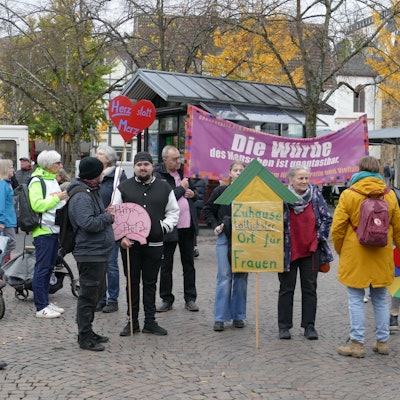 Menschen mit Protestplakaten und einem Transparent auf einem öffentlichen Platz.