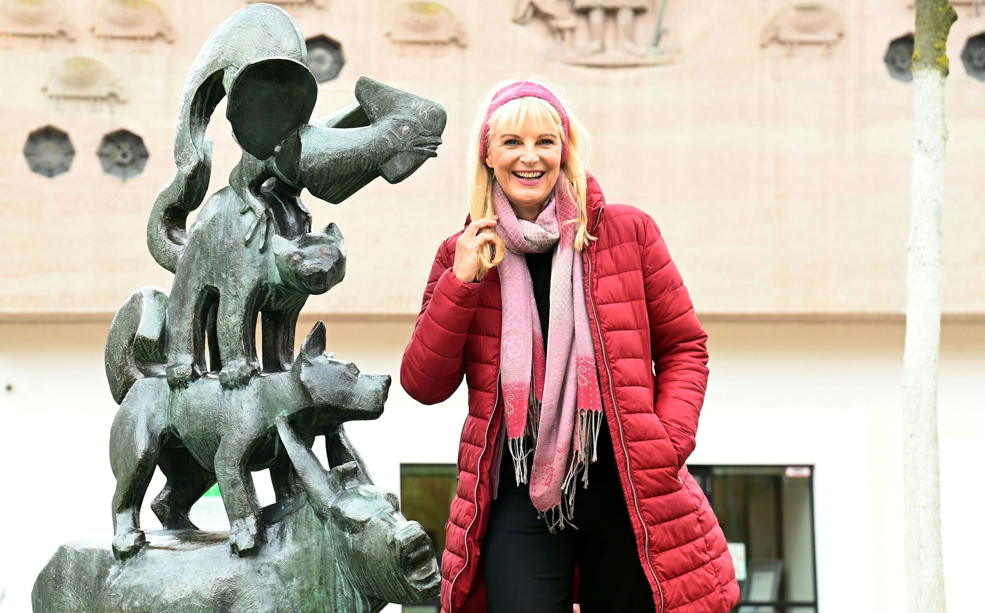 Eine Frau im roten Steppmantel steht neben einer Skulptur der Bremer Stadtmusikanten.