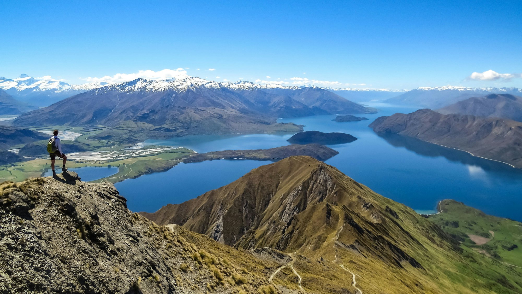 Ein Mann ist von hinten zu sehen, wie er auf eine Landschaft mit Seen und Bergen in Wanaka in Neuseeland schaut.