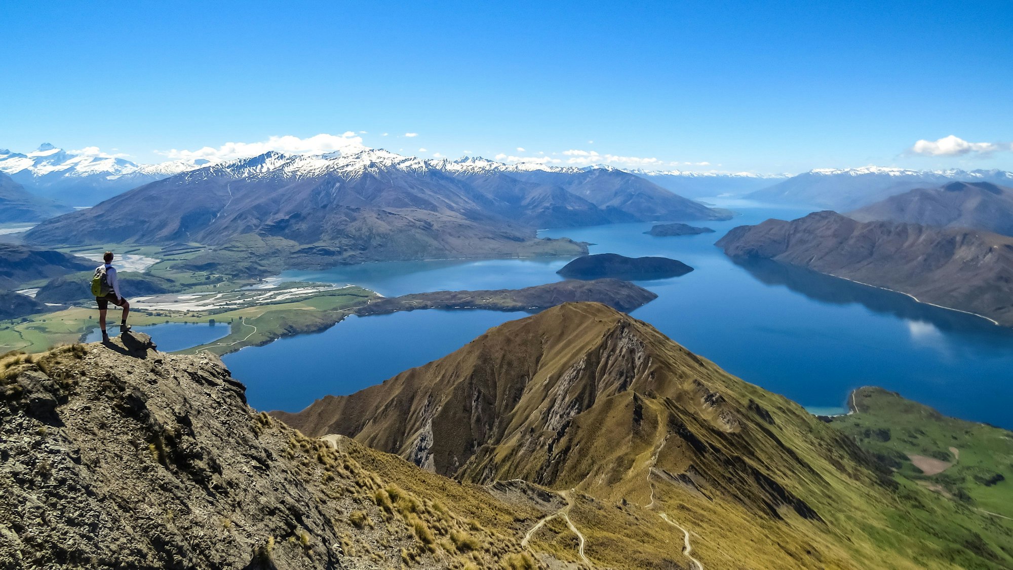 Ein Mann ist von hinten zu sehen, wie er auf eine Landschaft mit Seen und Bergen in Wanaka in Neuseeland schaut.