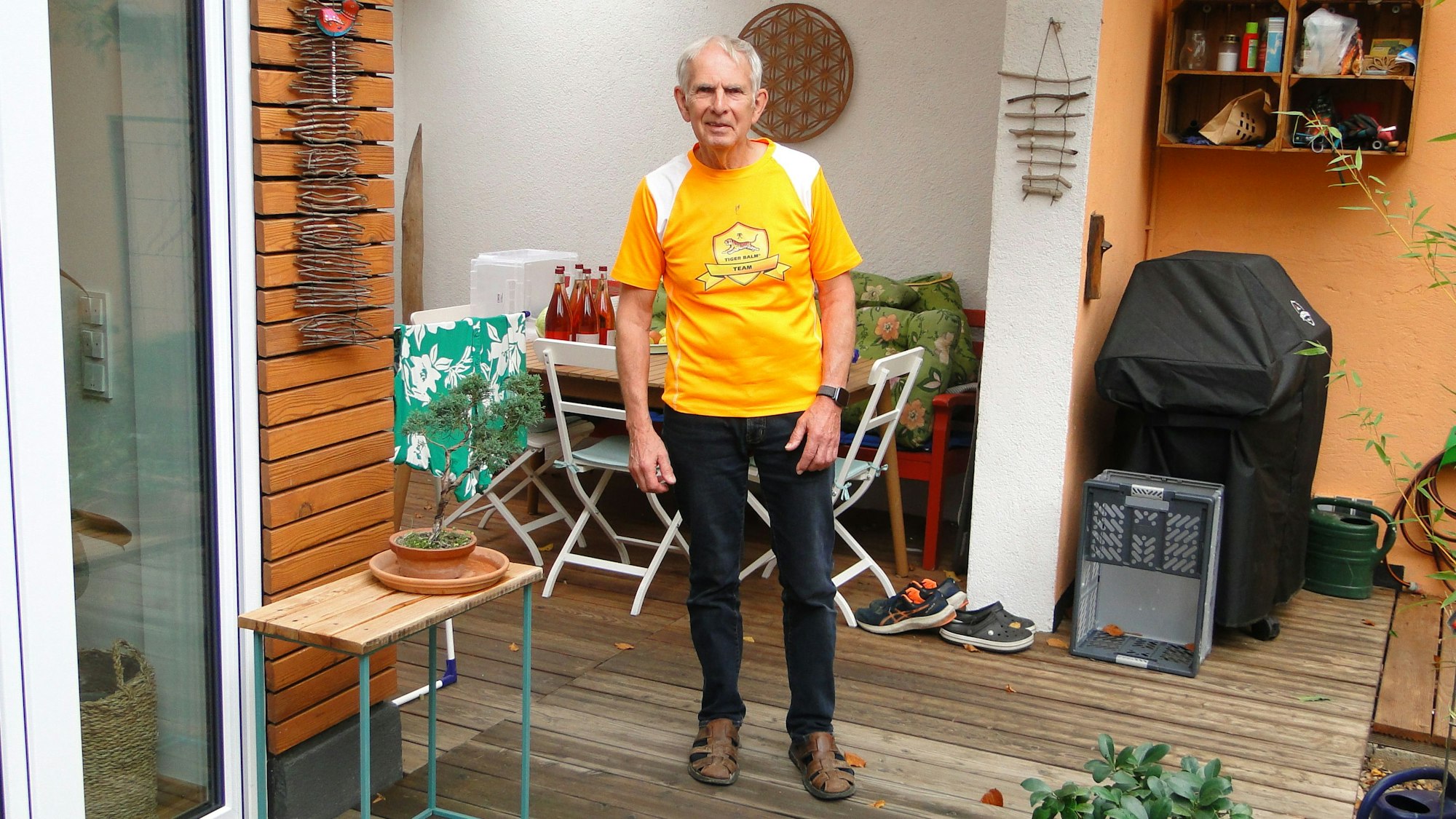 Ein Mann im orangen Shirt steht auf einer Terrasse.
