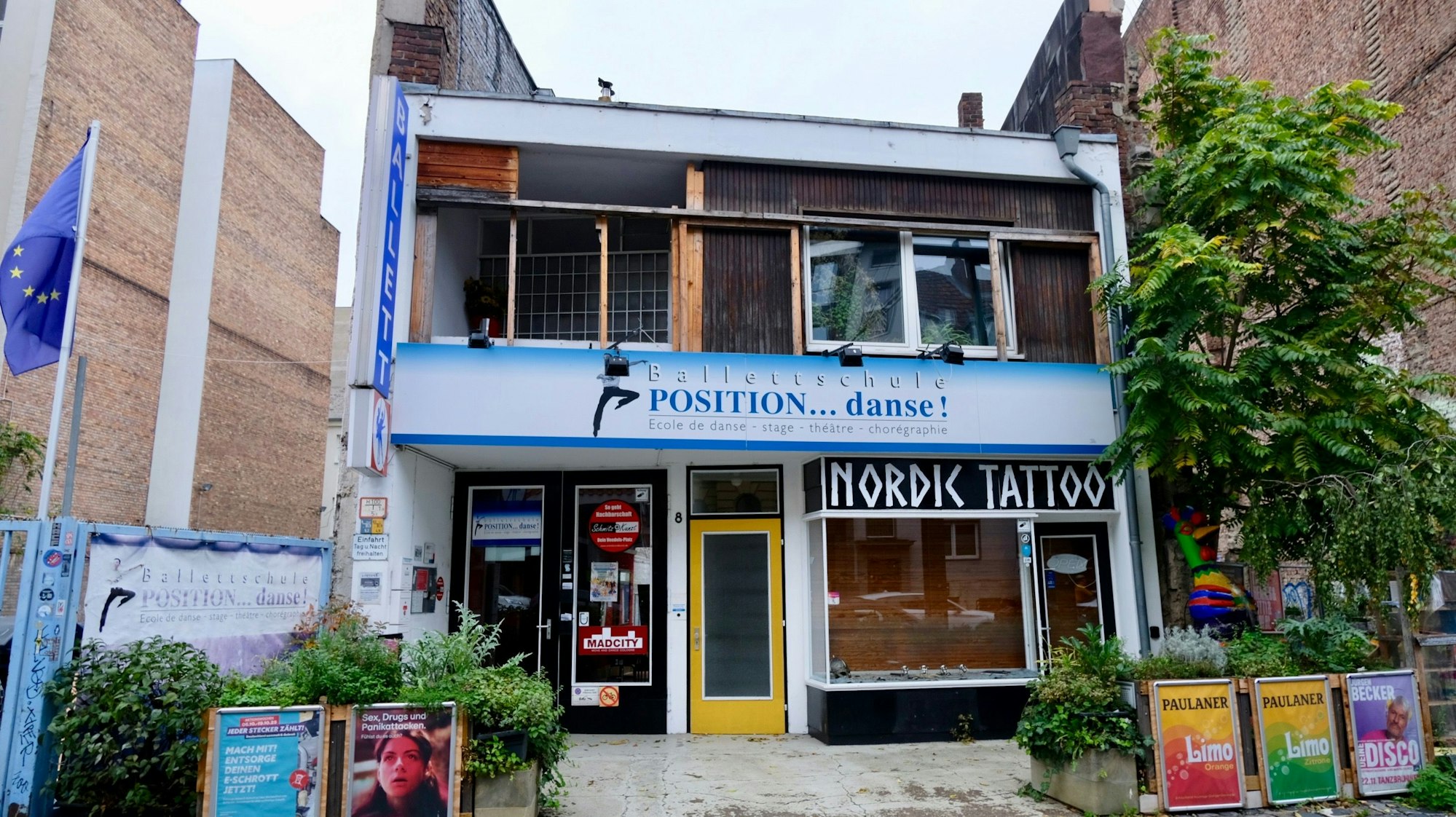 Ein zweigeschossiges würfelartiges Gebäude steht zwischen zwei Backsteingebäuden.