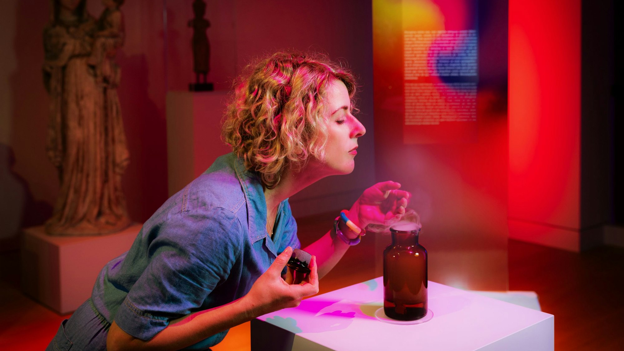 Eine Frau riecht intensiv an einer Flasche, die auf einem Podest im Museum Kunstpalast ausgestellt ist.