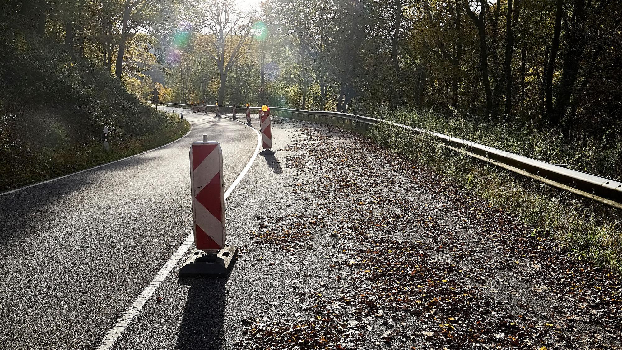 Die rechte Spur einer Straße ist mit Warnbaken abgesperrt. Auf der Fahrbahn liegt Laub.