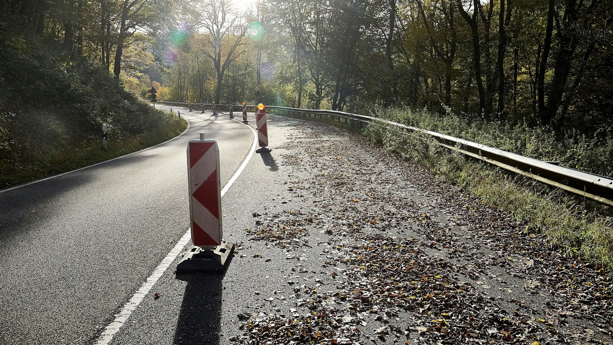 Die rechte Spur einer Straße ist mit Warnbaken abgesperrt. Auf der Fahrbahn liegt Laub.