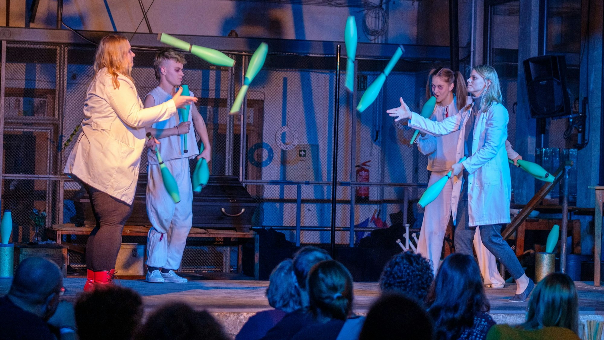 Junge Leute in weißen Kitteln werfen sich Jonglierkeulen zu.