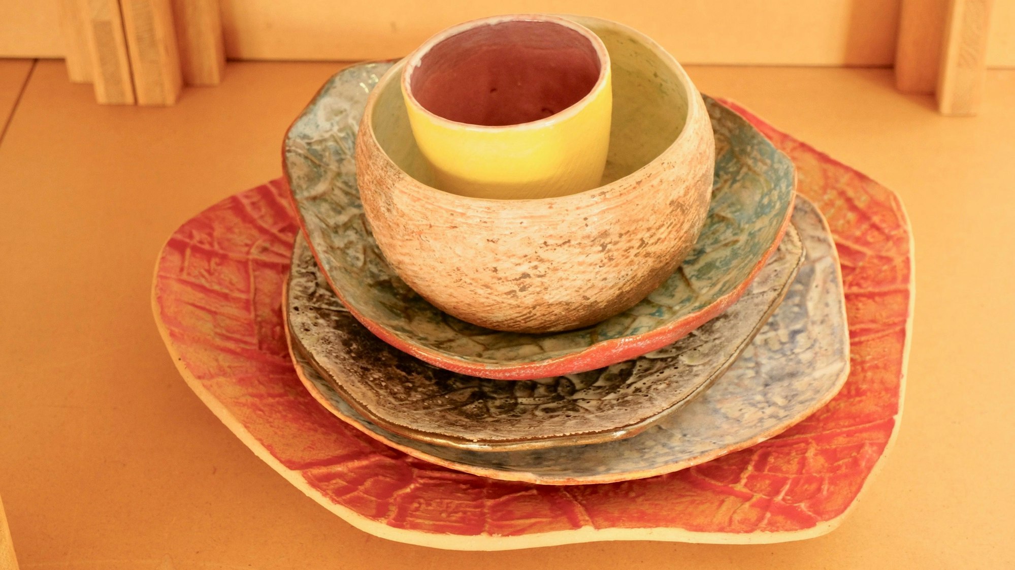 Keramikteller in verschiedenen Größen und Farben sind übereinander gestapelt. Ganz oben ist eine Schale platziert, so dass das Ganze an eine Blüte erinnert.