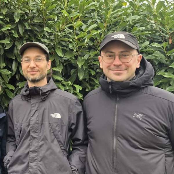 Drei Männer und eine Frau stehen nebeneinander vor einer grünen Hecke,