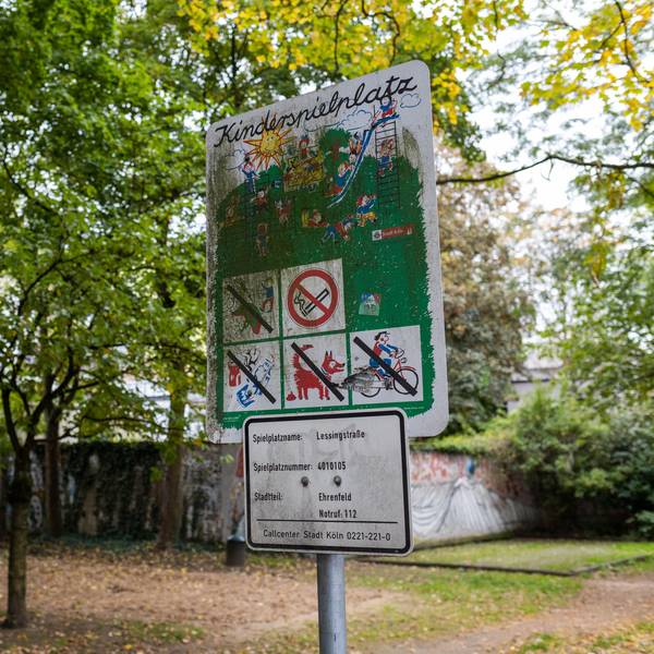 Ein Spielplatzschild steht vor einem leeren Spielplatz.