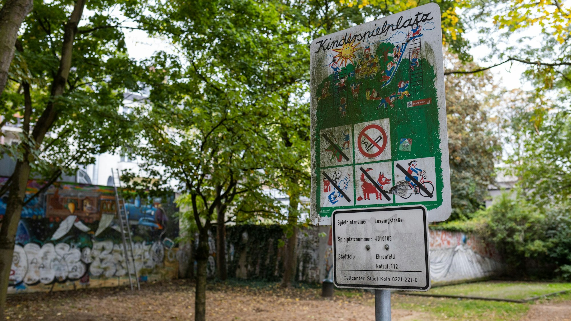 Ein Spielplatzschild steht vor einem leeren Spielplatz.