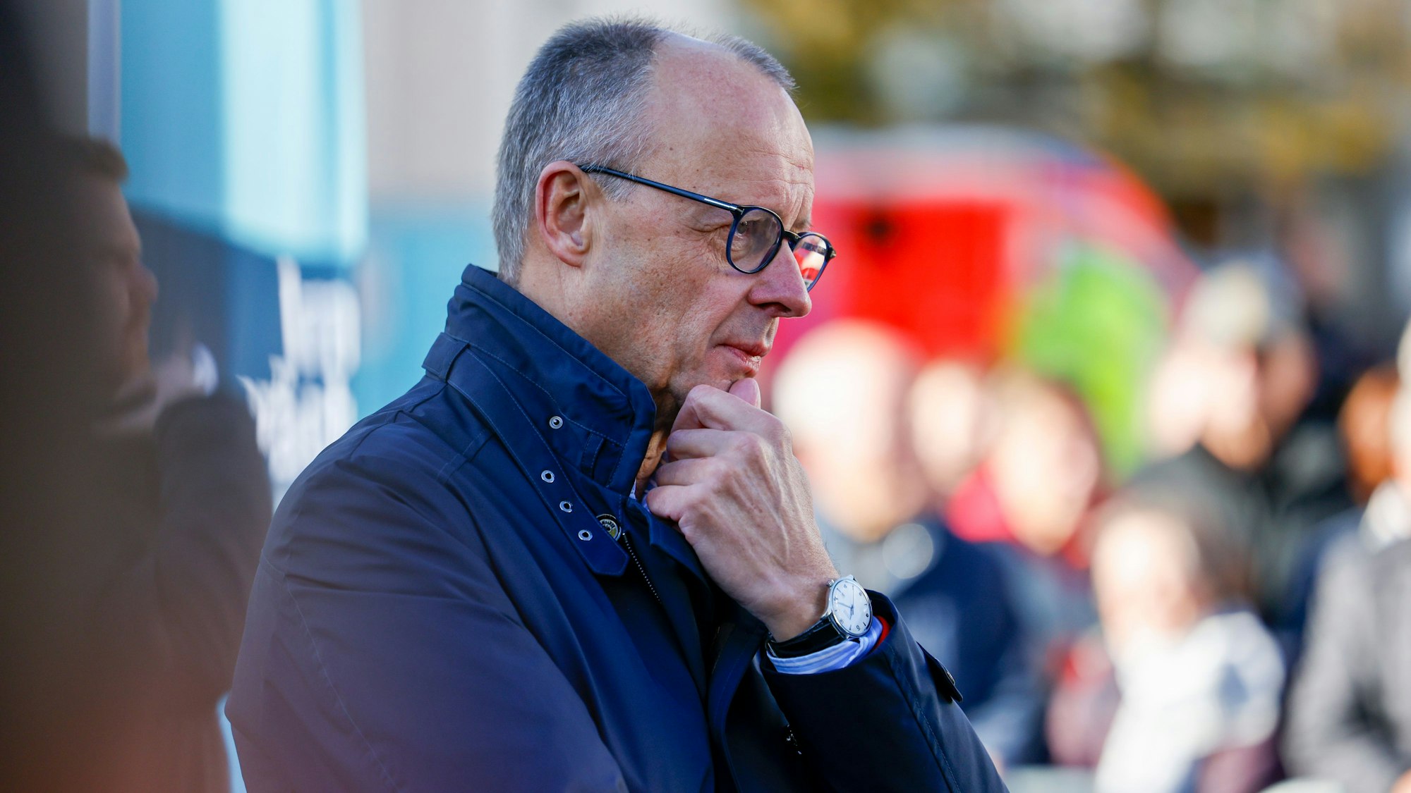 Bundeskanzler Friedrich Merz (CDU) hört sich bei einem Bürgergespräch in Meschede Fragen der Zuschauer an. Er sieht nachdenklich aus, berührt mit einer Hand sein Kinn.