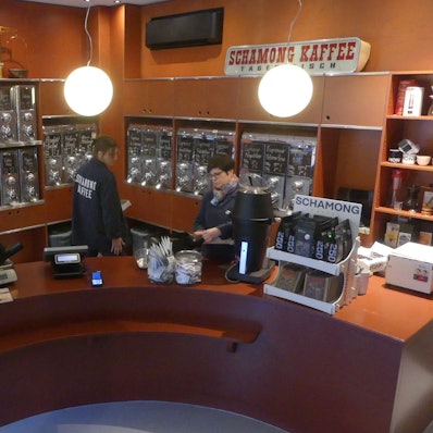 Blick in den Verkaufsraum einer Kaffee-Rösterei mit halbrundem Verkaufstresen und vielen Kaffeebohnen-Behältern an der Wand